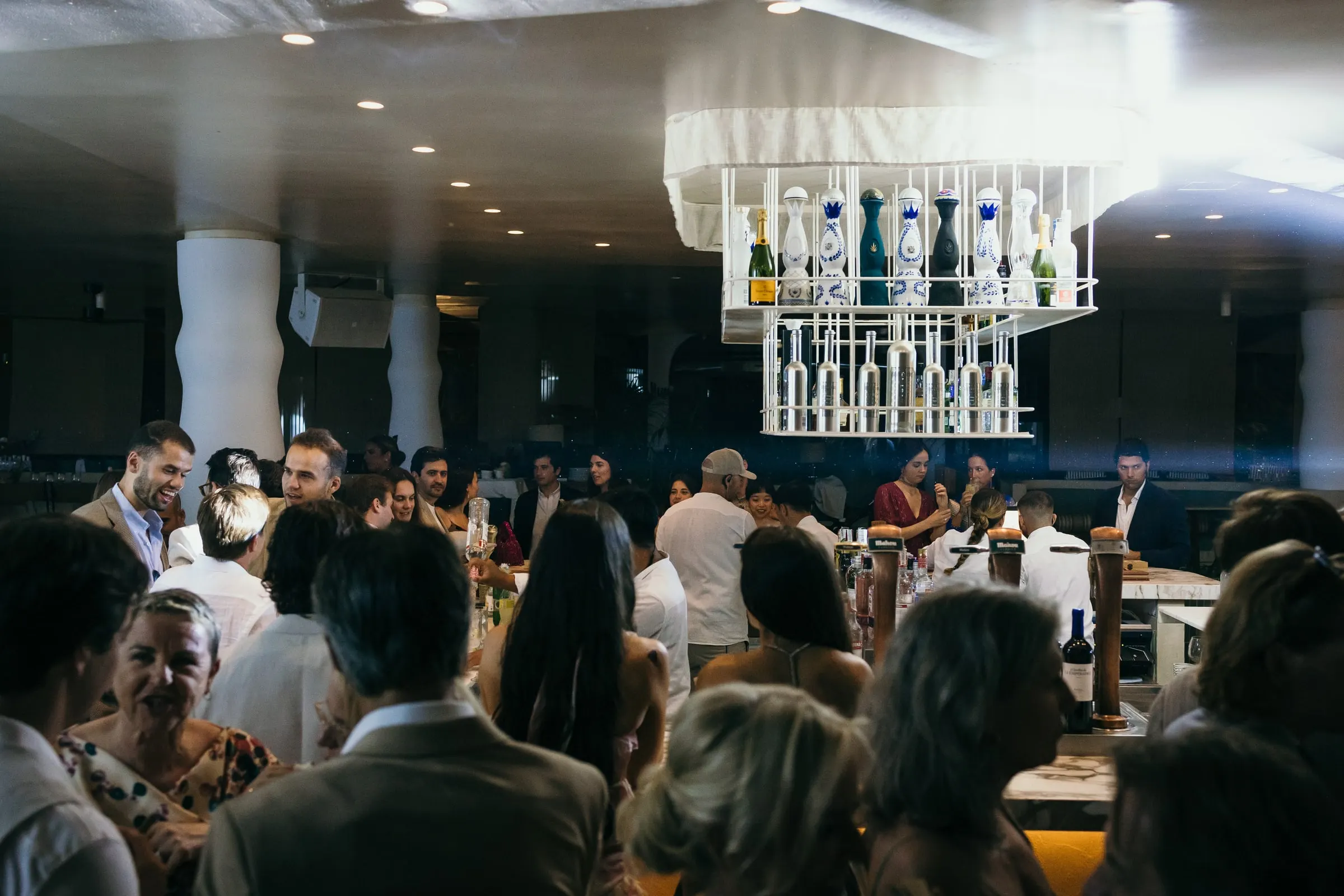Guests chatting at the bar under a chandelier of hanging bottles, Barbillón, Marbella