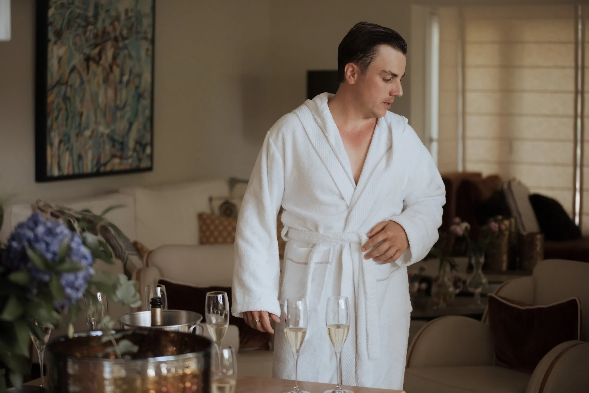 Groom in a white bathrobe beside champagne glasses and blue hydrangeas on the morning of his wedding at Barbillón, Marbella