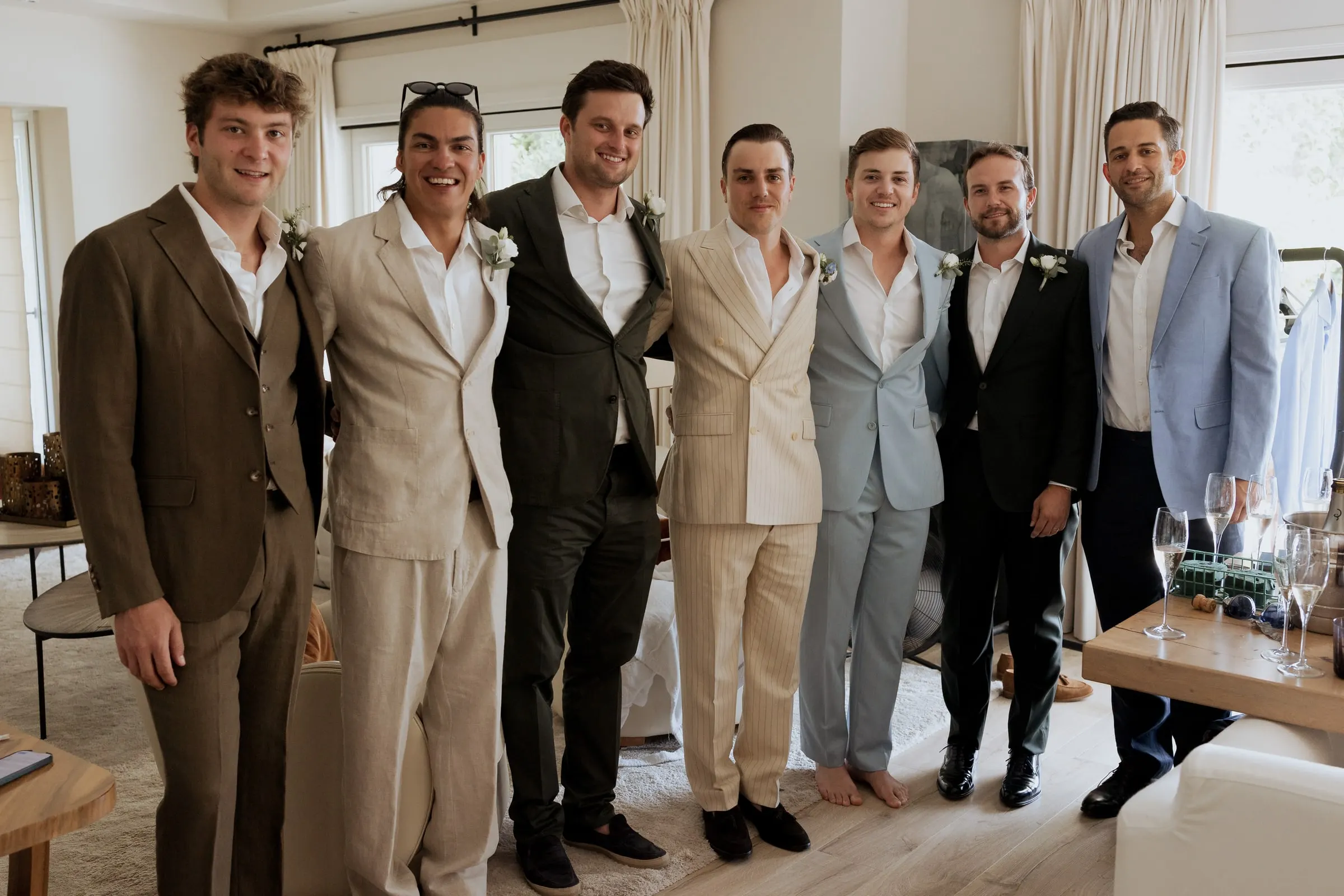 Groom and his six groomsmen in suits of different colours lined up in a living room before the wedding at Barbillón, Marbella