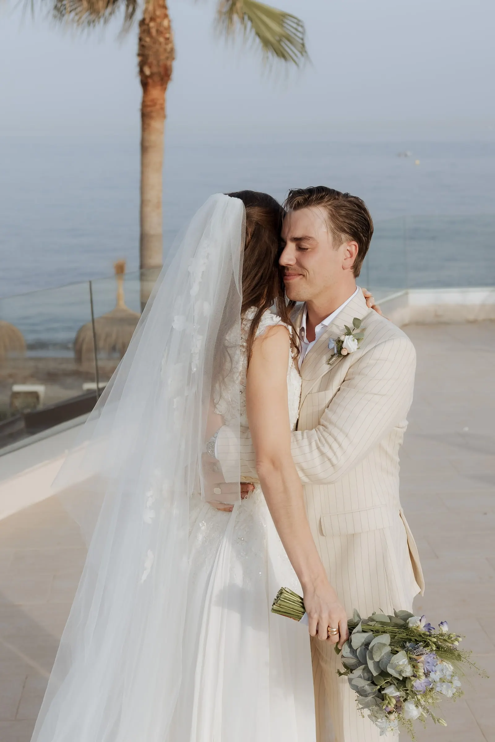 Bride and groom in a close embrace on the terrace with a palm tree behind, at Barbillón, Marbella