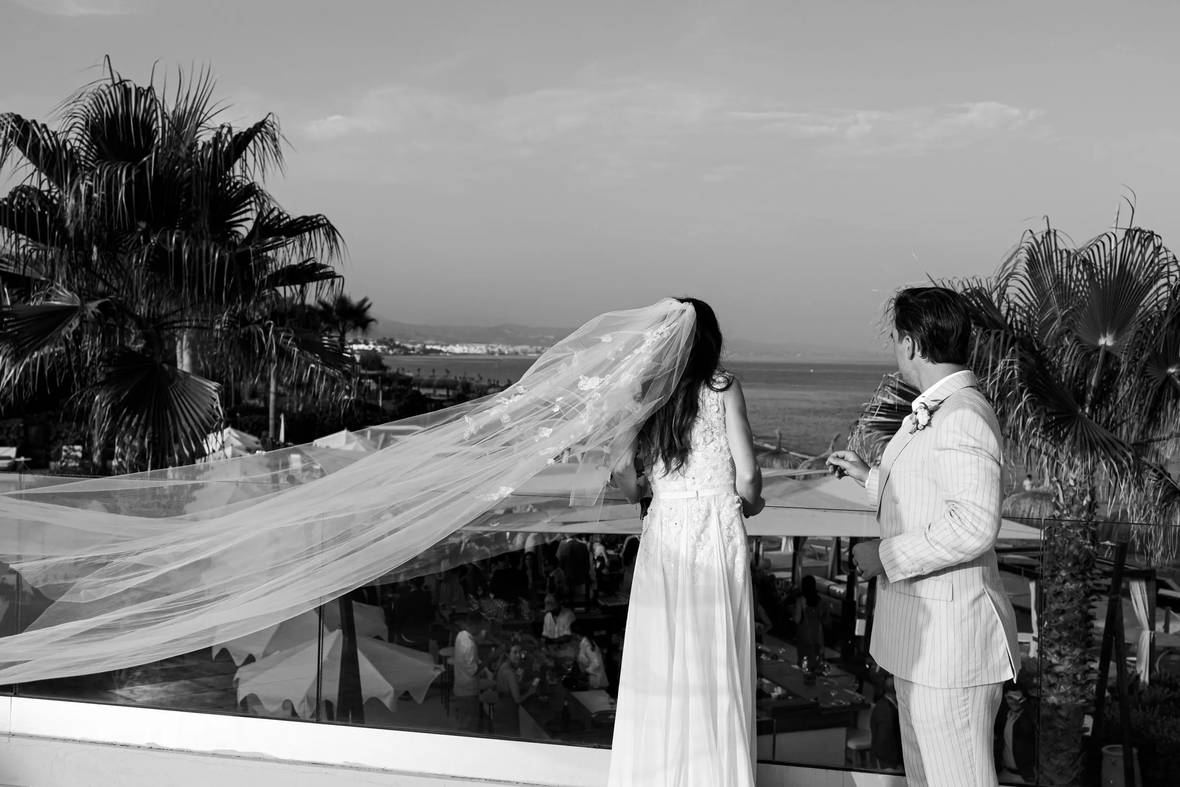 Black and white of the bride's long veil blowing in the wind beside the groom, Barbillón, Marbella