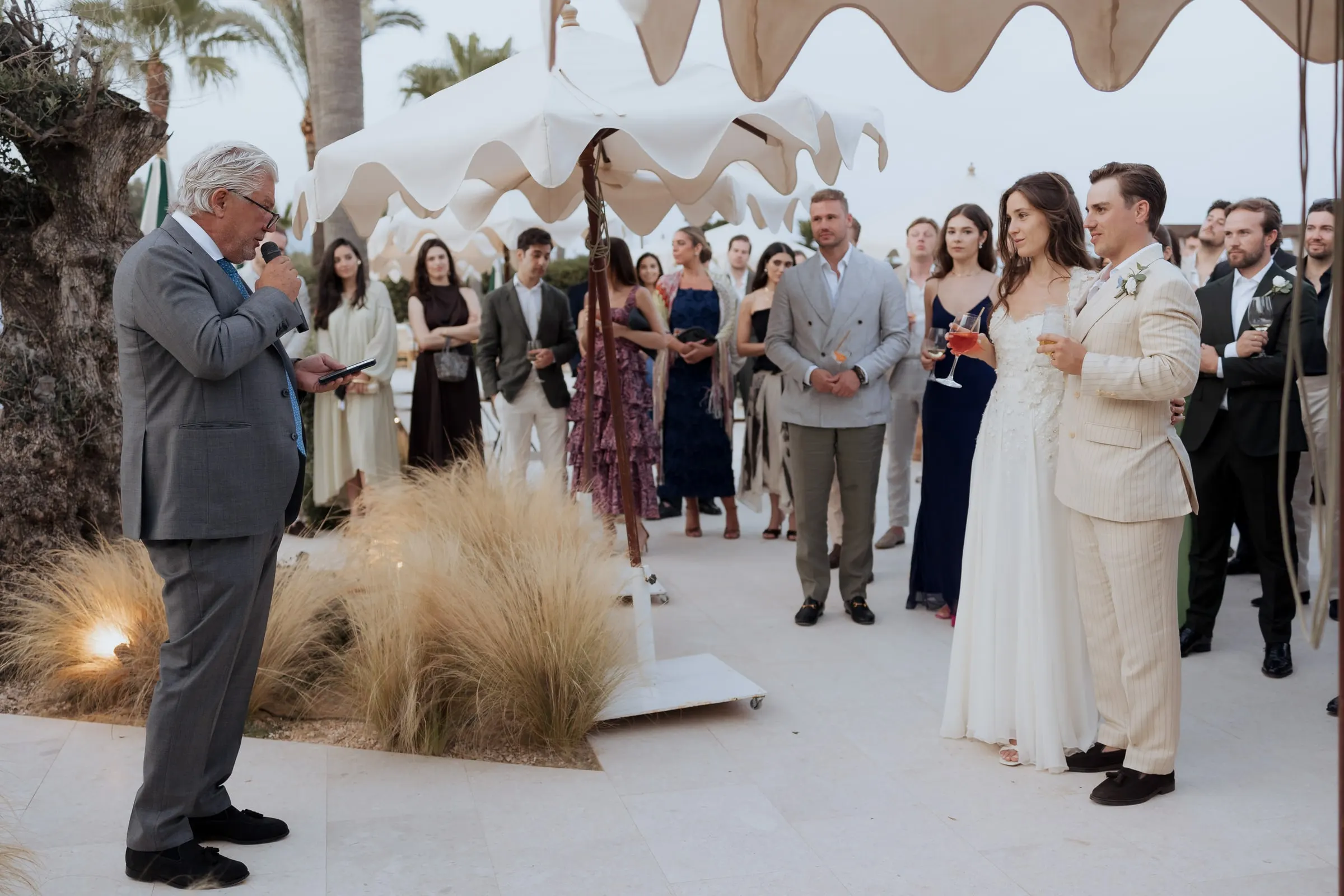 Guest giving a speech while the bride, groom and guests listen under white scalloped umbrellas at Barbillón, Marbella