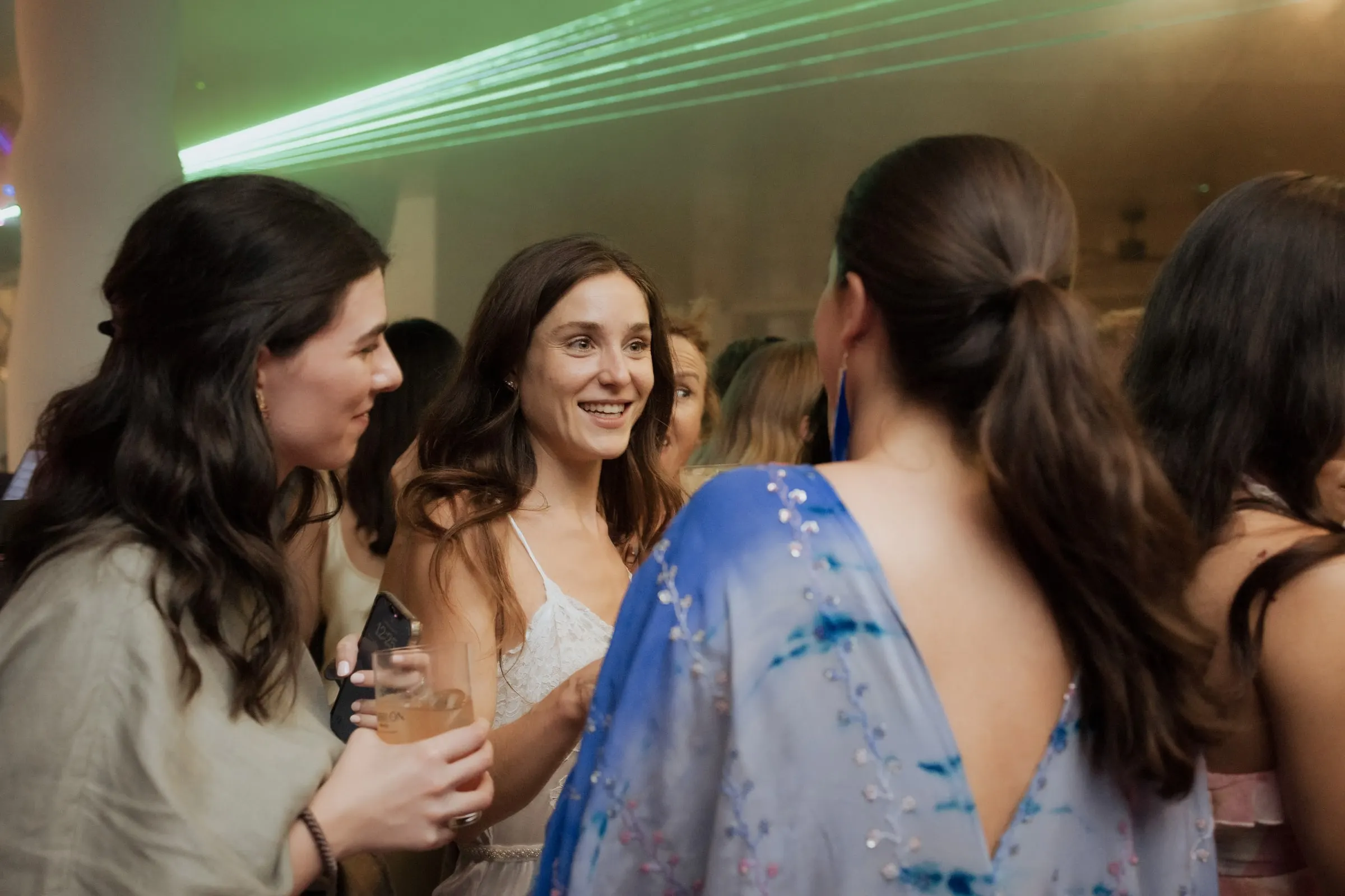 Bride smiling among friends with drinks under green party lights at Barbillón, Marbella