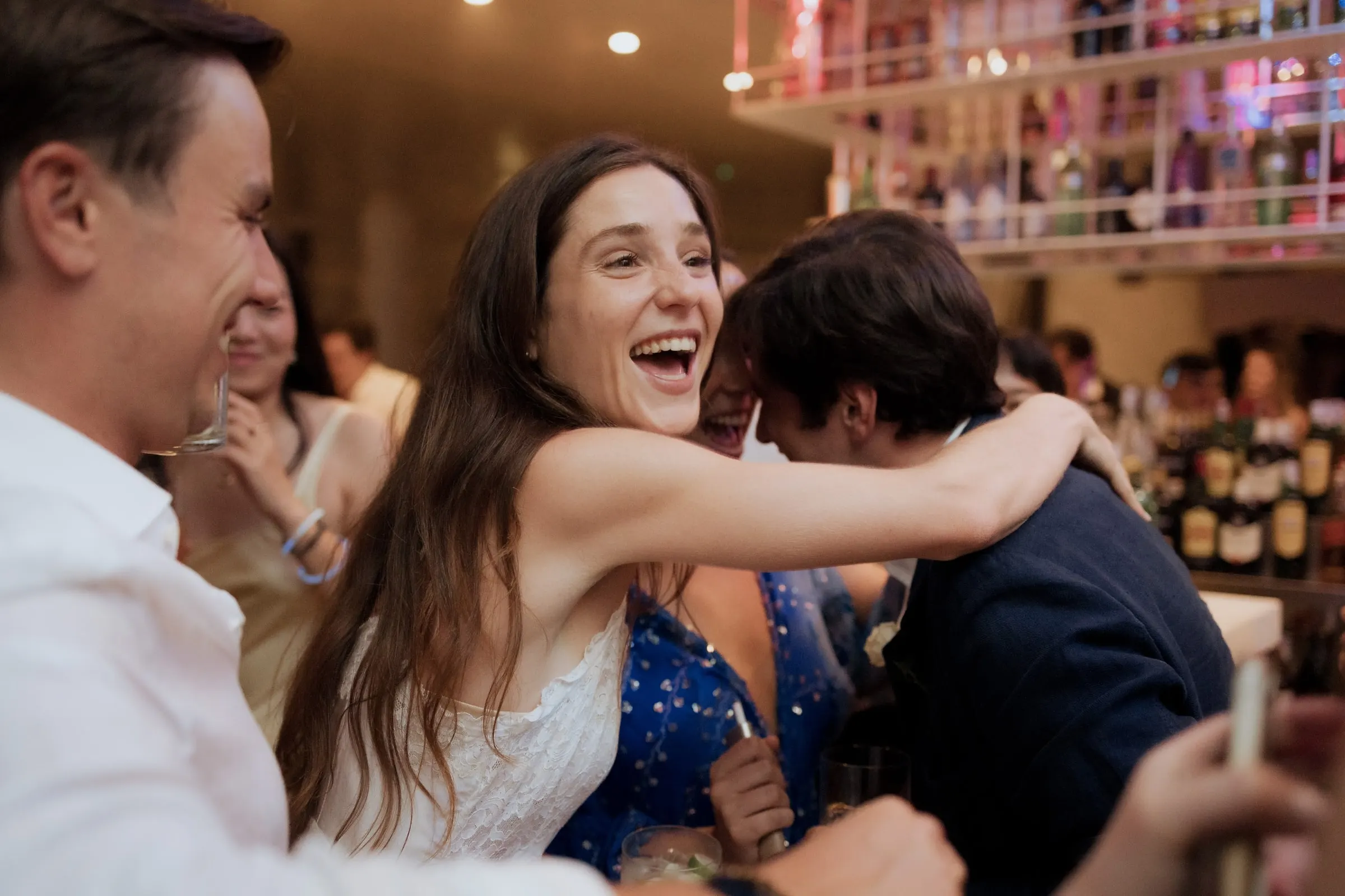 Bride laughing as she hugs a guest at the party, with the bar shelves behind, at Barbillón, Marbella