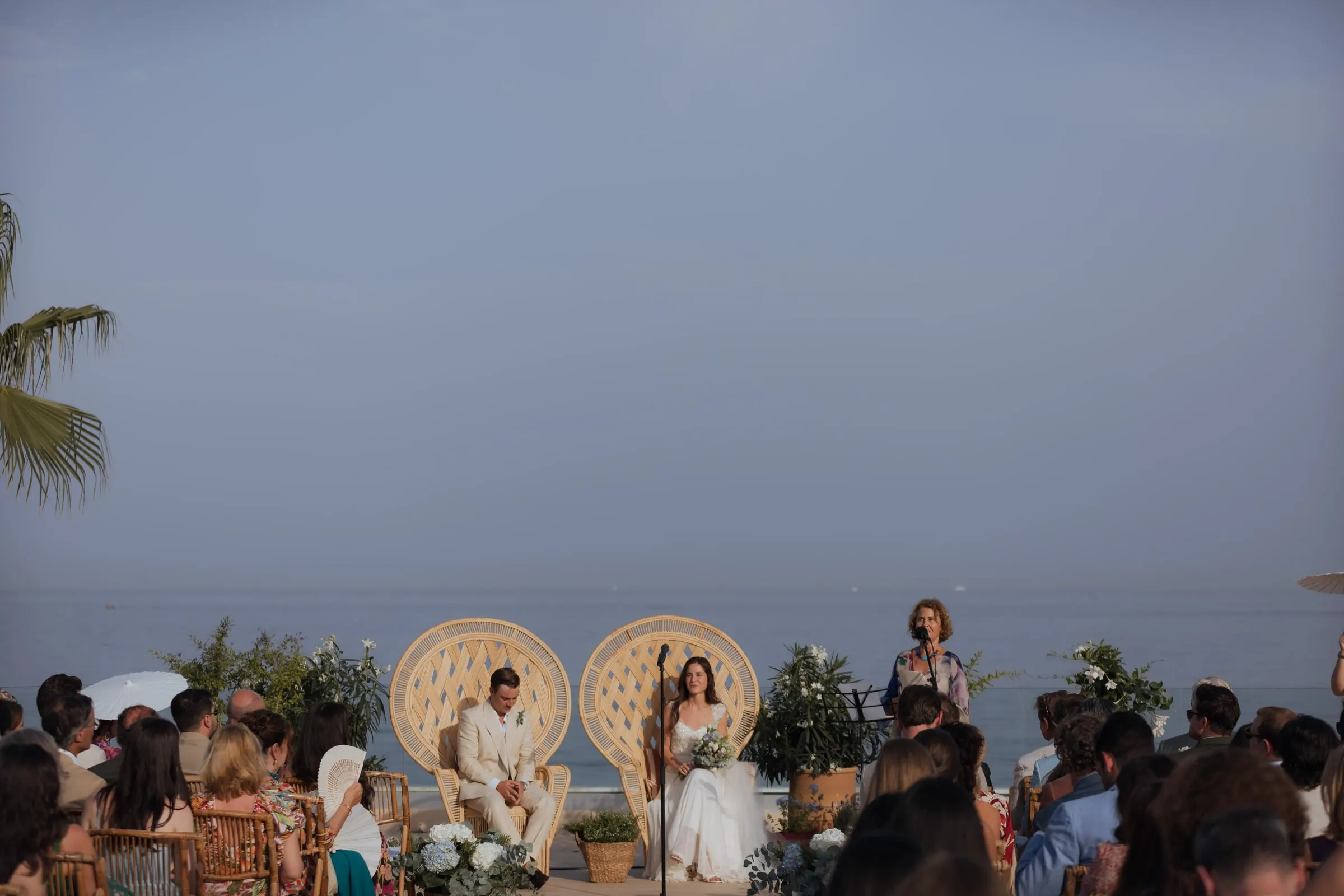 Ceremony by the sea with the couple in wicker peacock chairs facing the guests, Barbillón, Marbella