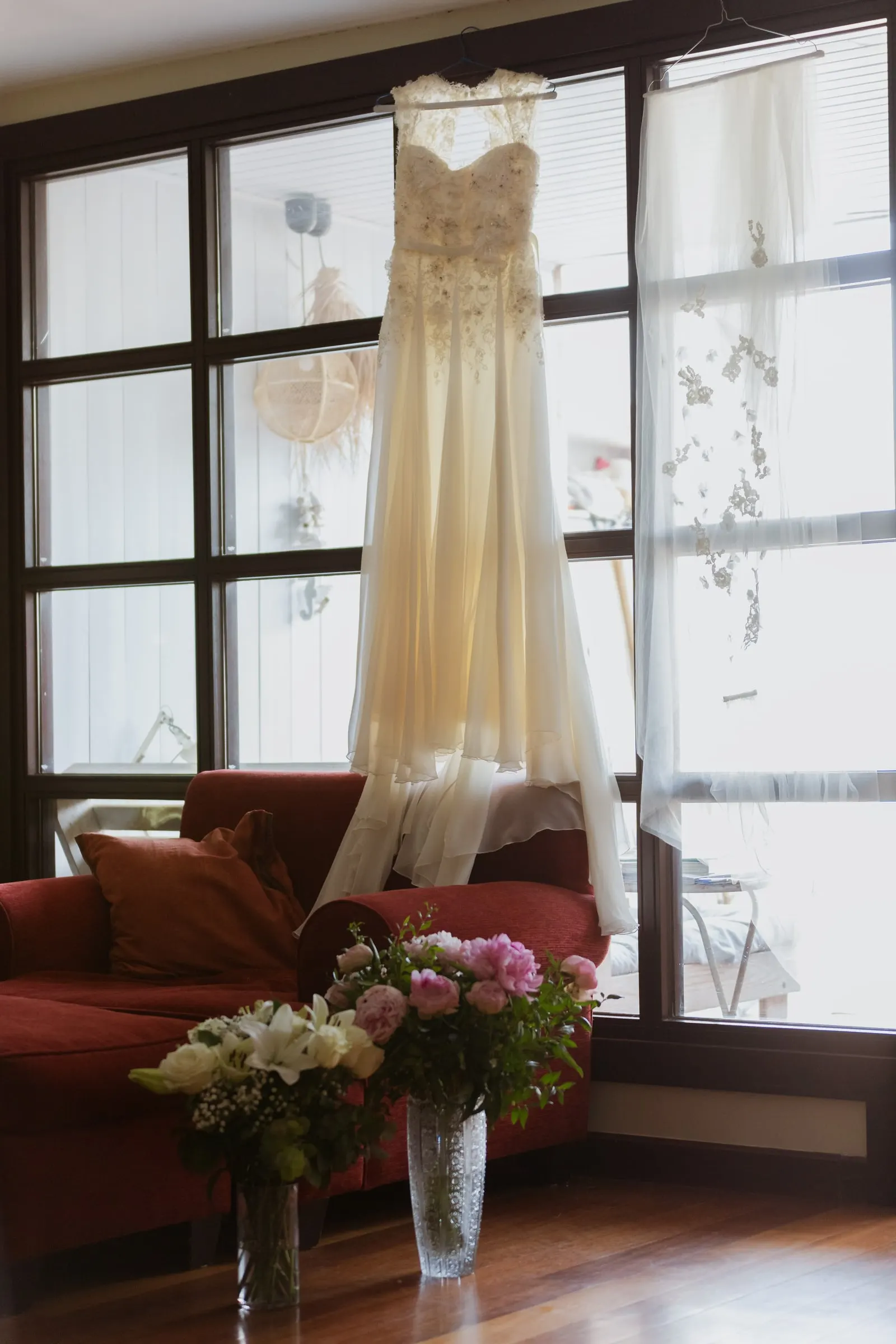 Wedding dress hanging at the window above vases of peonies, Barbillón, Marbella