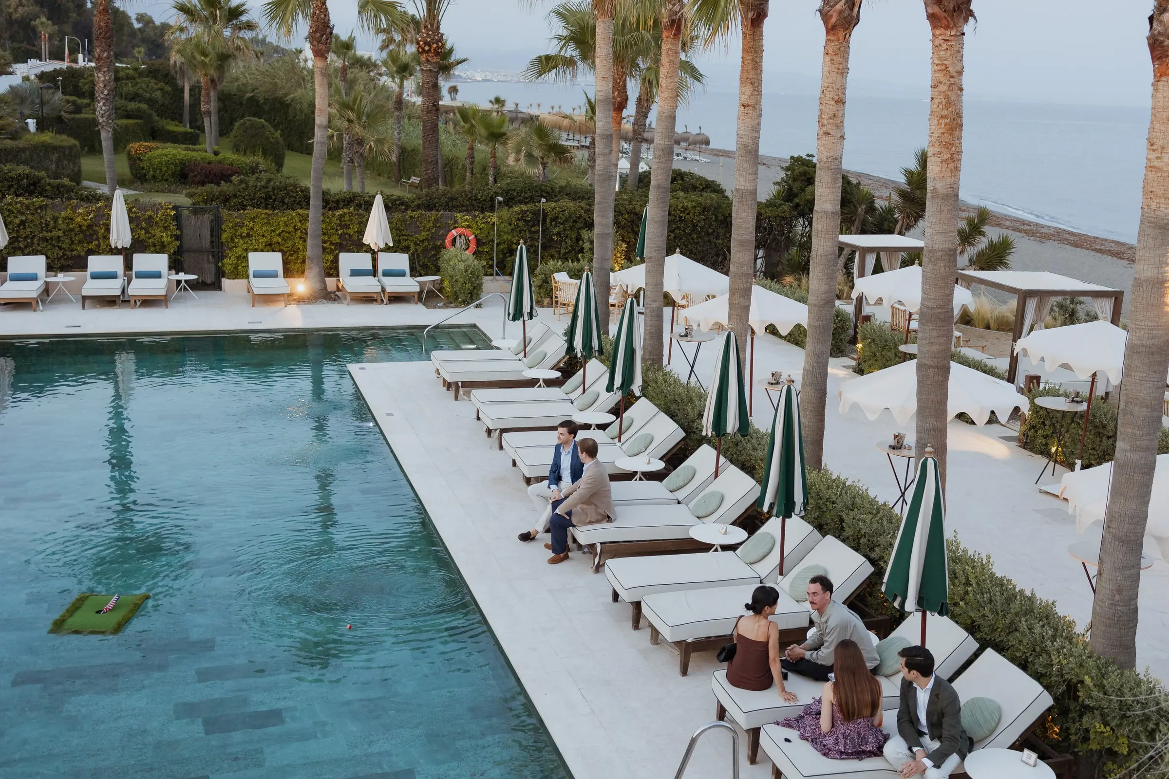 High view of the pool, palms and sunbeds as guests chat, Barbillón, Marbella
