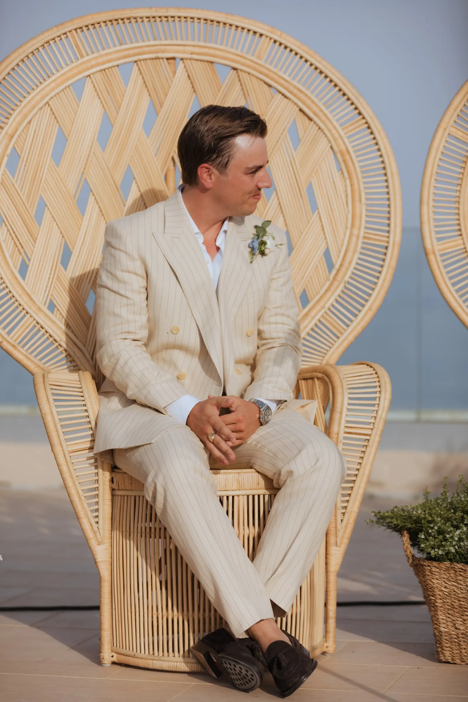 Groom seated in a wicker peacock chair at the ceremony by the sea, Barbillón, Marbella