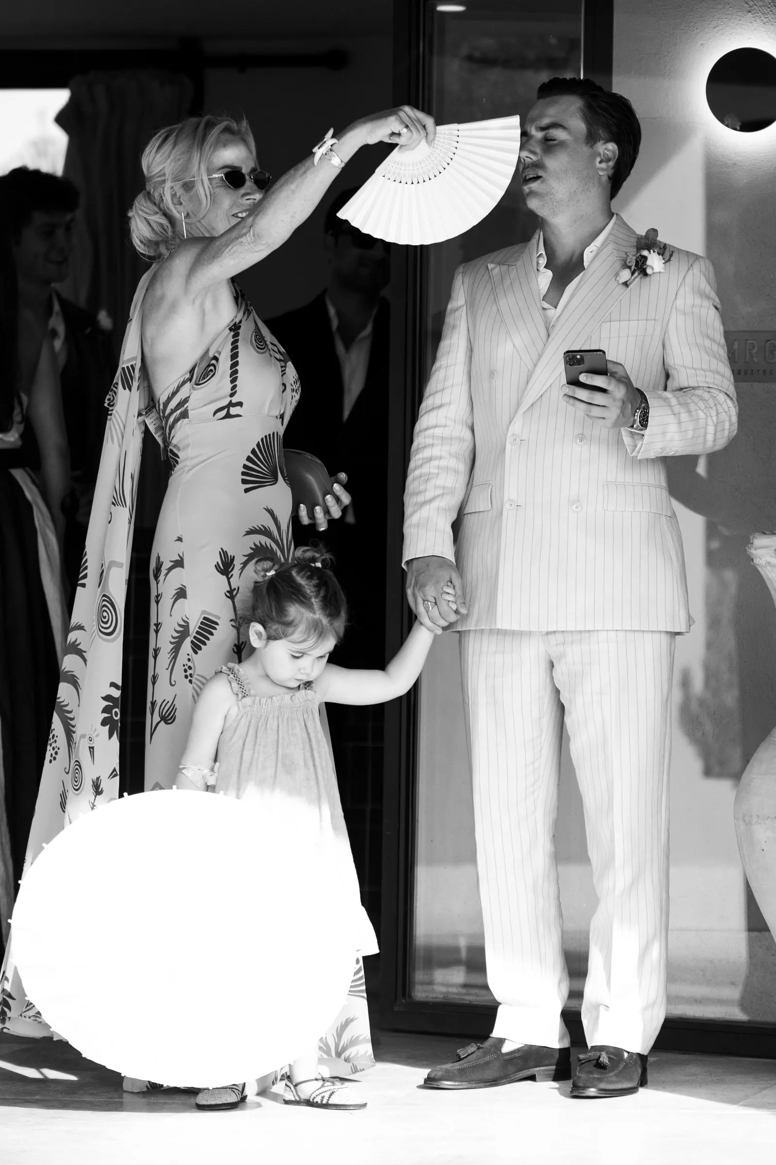 Black and white of a woman fanning the groom as a little girl holds his hand, Barbillón, Marbella