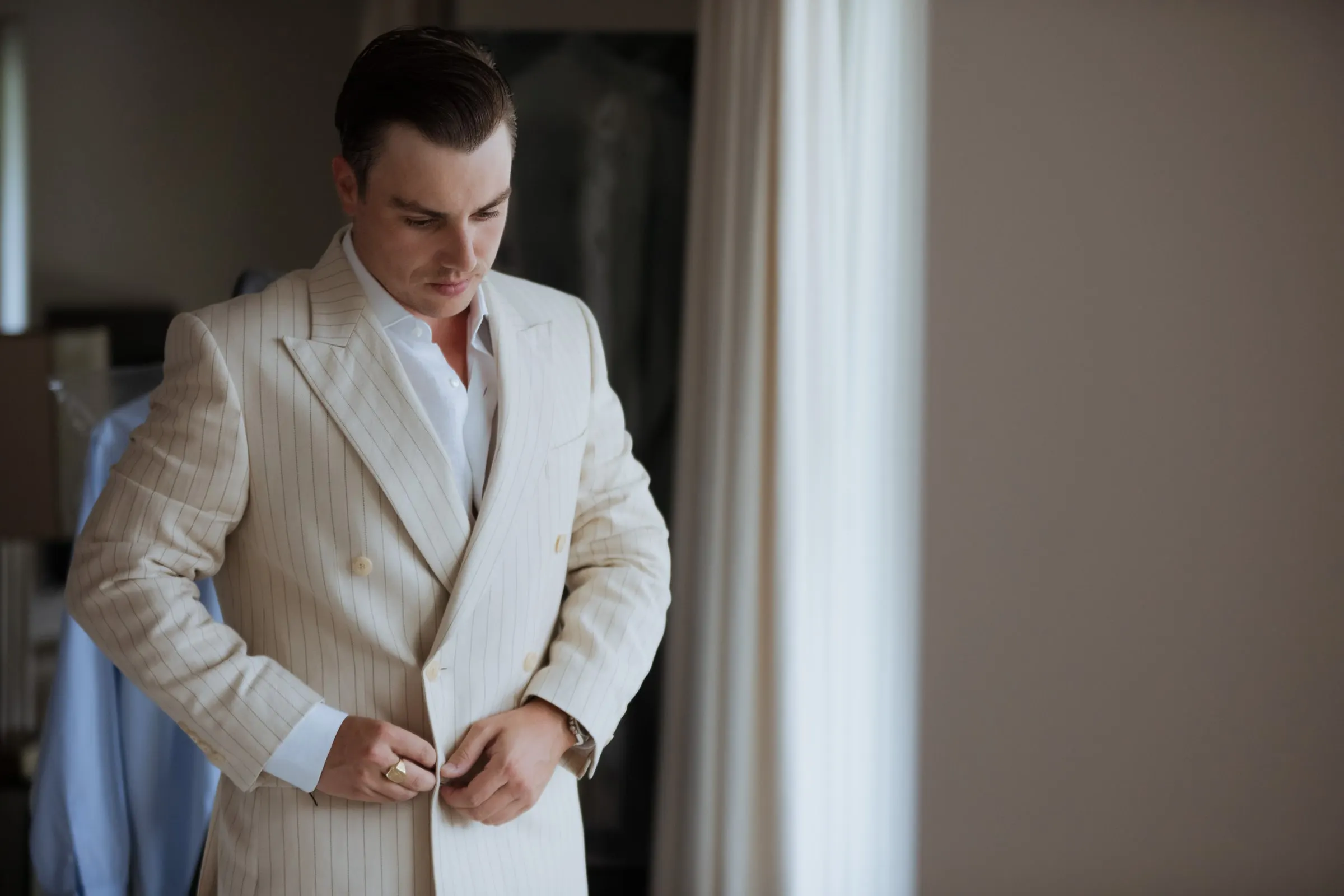 Groom fastening his double-breasted cream jacket by the window, Barbillón, Marbella
