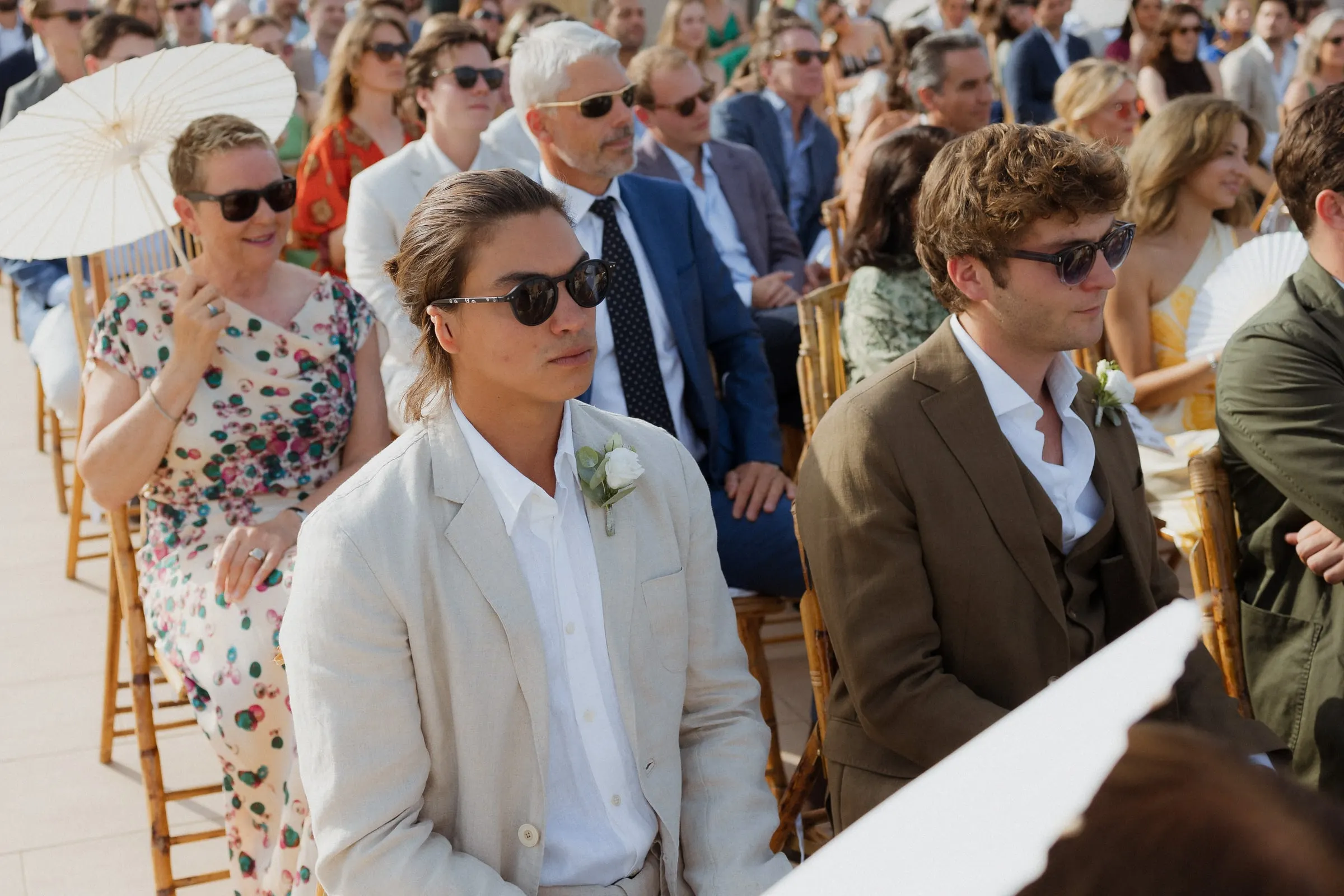 Guests in sunglasses seated on wooden chairs during the ceremony, Barbillón, Marbella