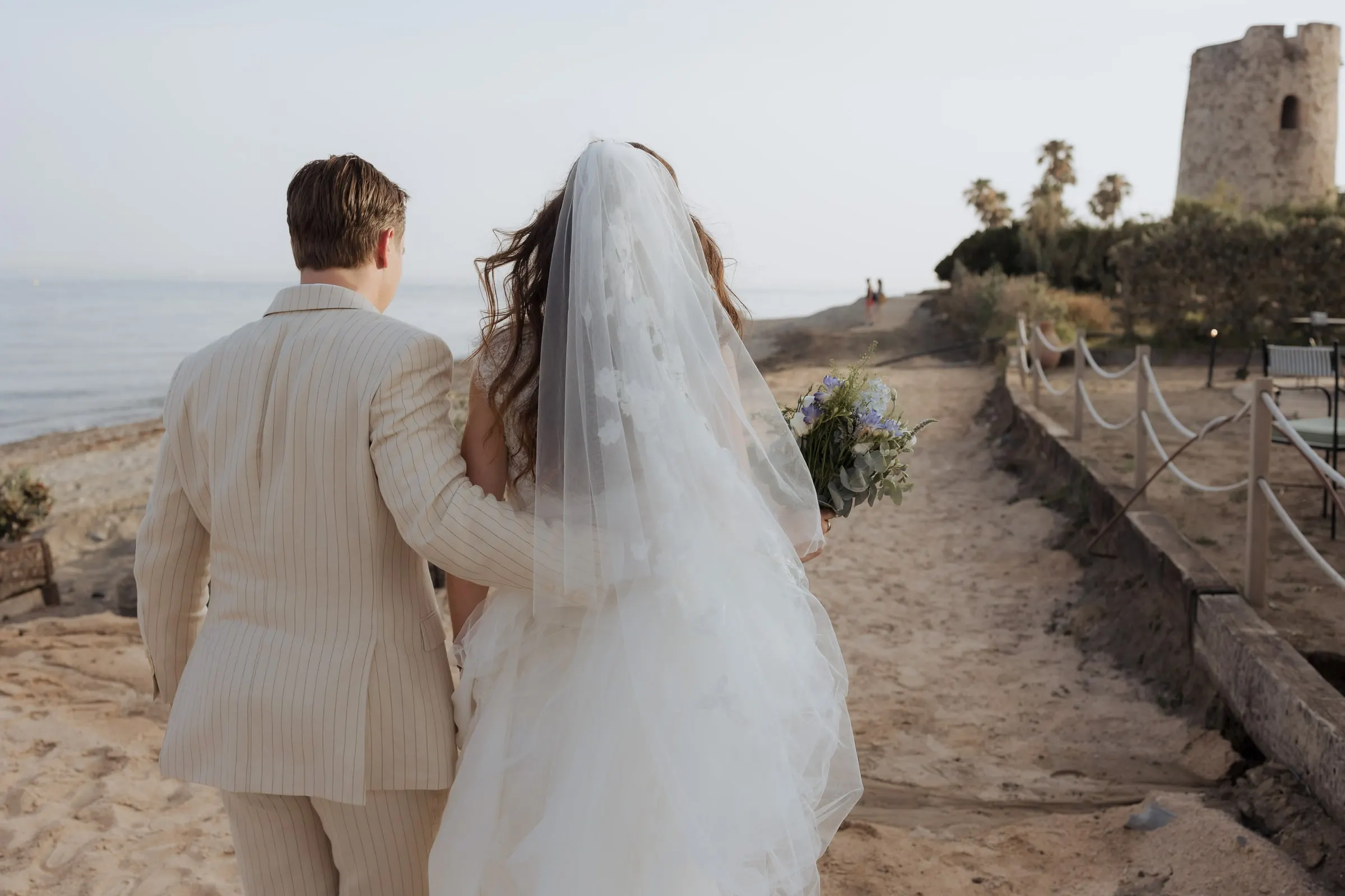 Couple walking along a sandy path towards an old watchtower, seen from behind, Barbillón, Marbella