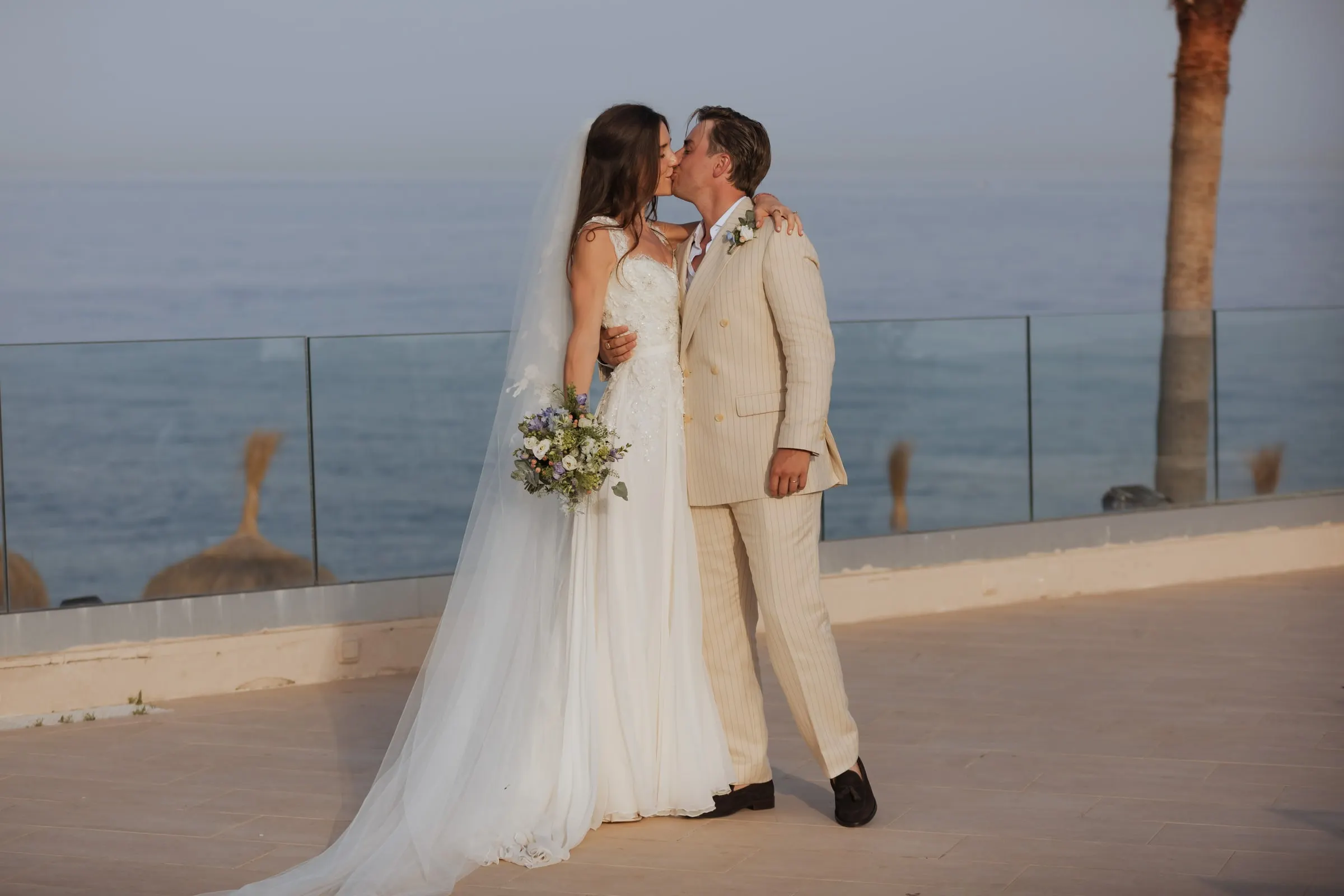 Bride and groom kissing on the terrace with the sea behind the glass railing, Barbillón, Marbella