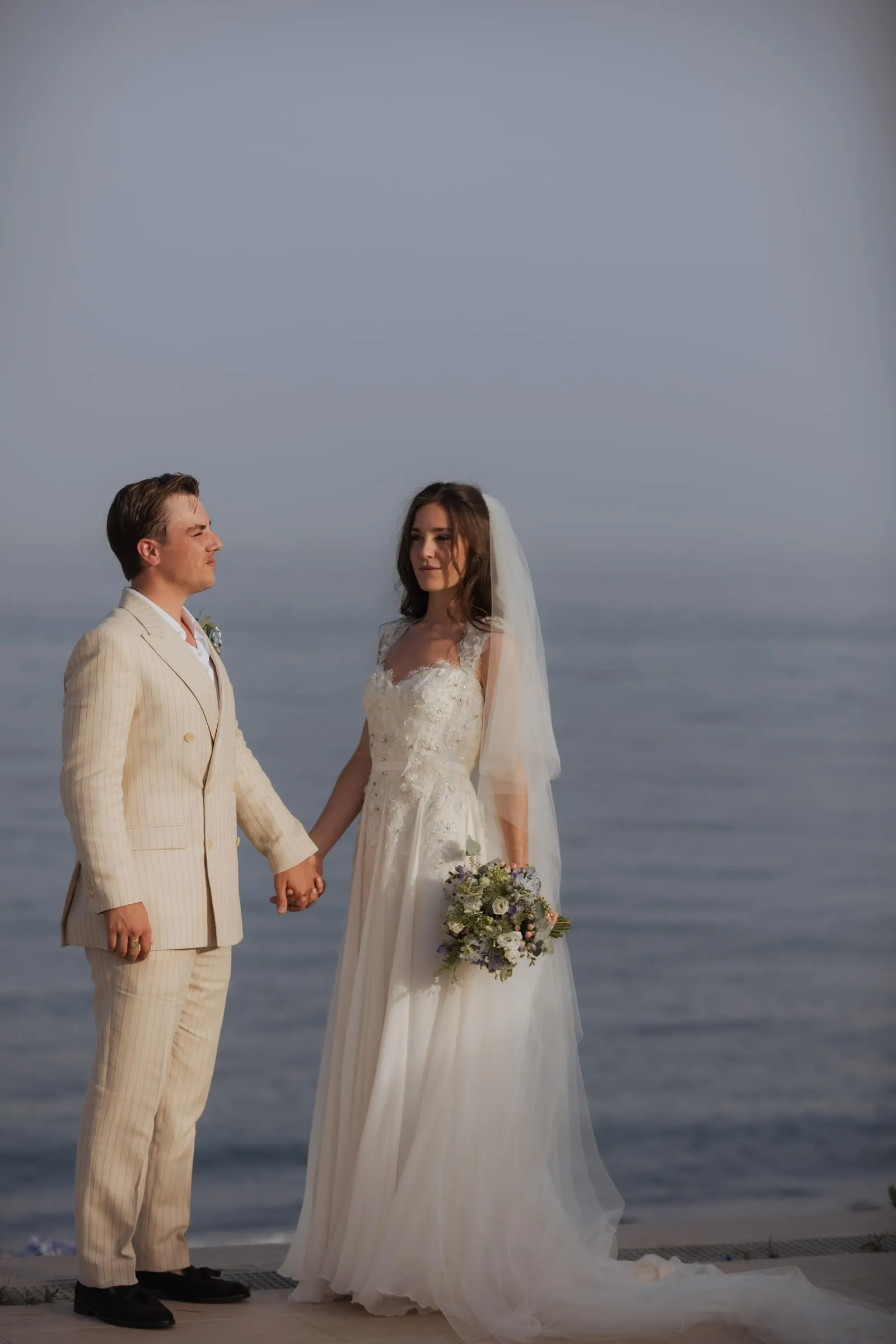 Bride and groom holding hands, gazing at each other in front of the sea, Barbillón, Marbella