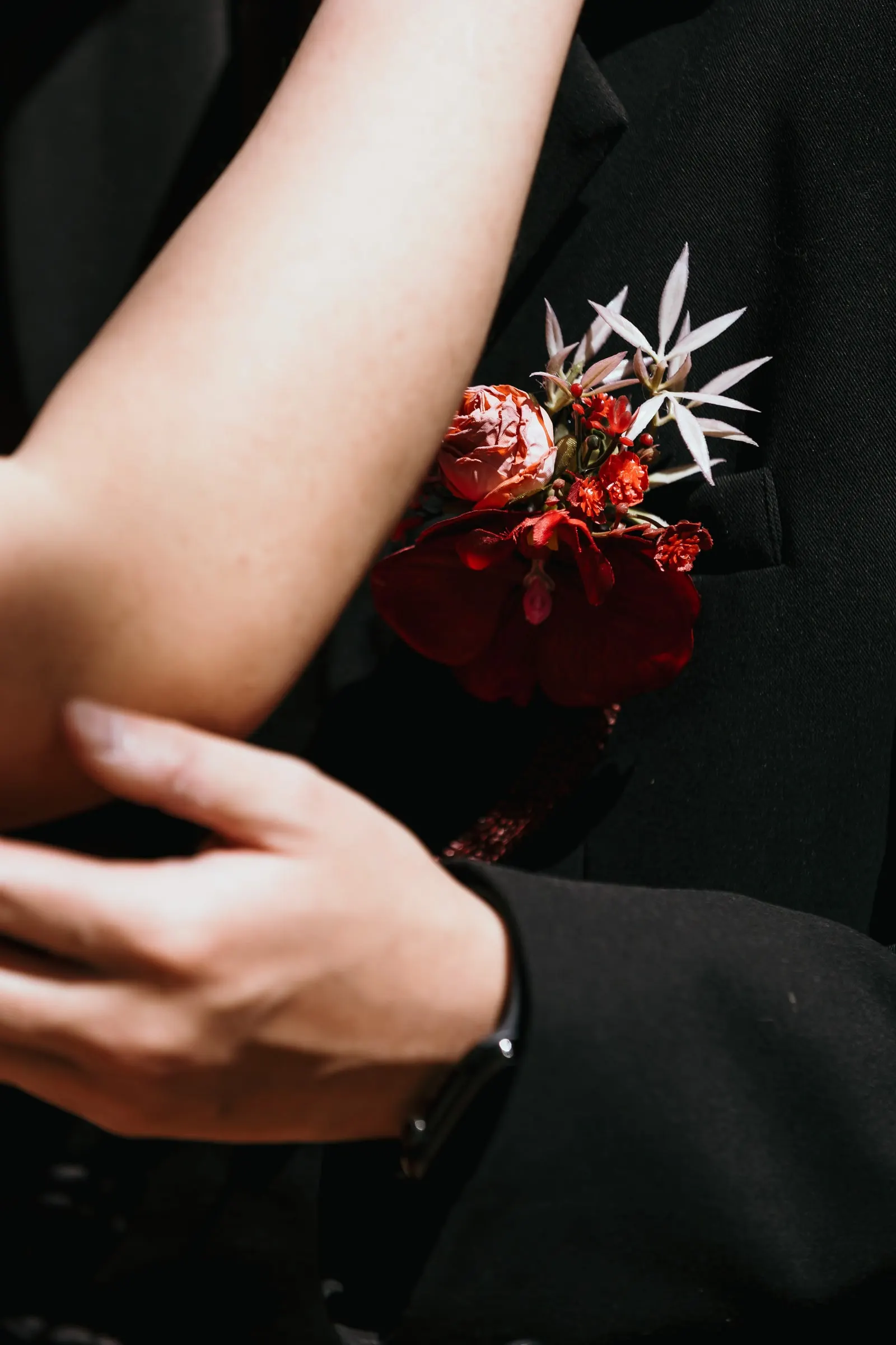 Close-up of her hand on his black sleeve and his red flower boutonnière, pre-wedding session in Alhaurín de la Torre