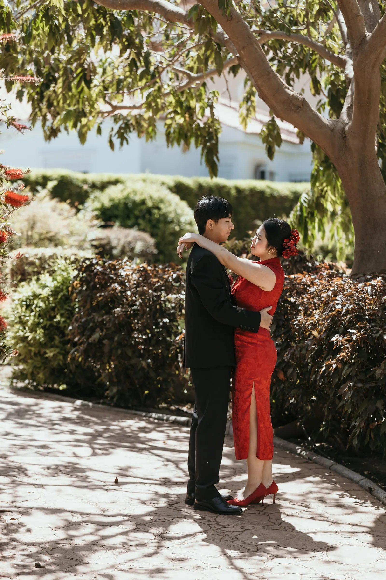 Bride-to-be with her arms around her fiancé’s neck under a tree in the Japanese garden