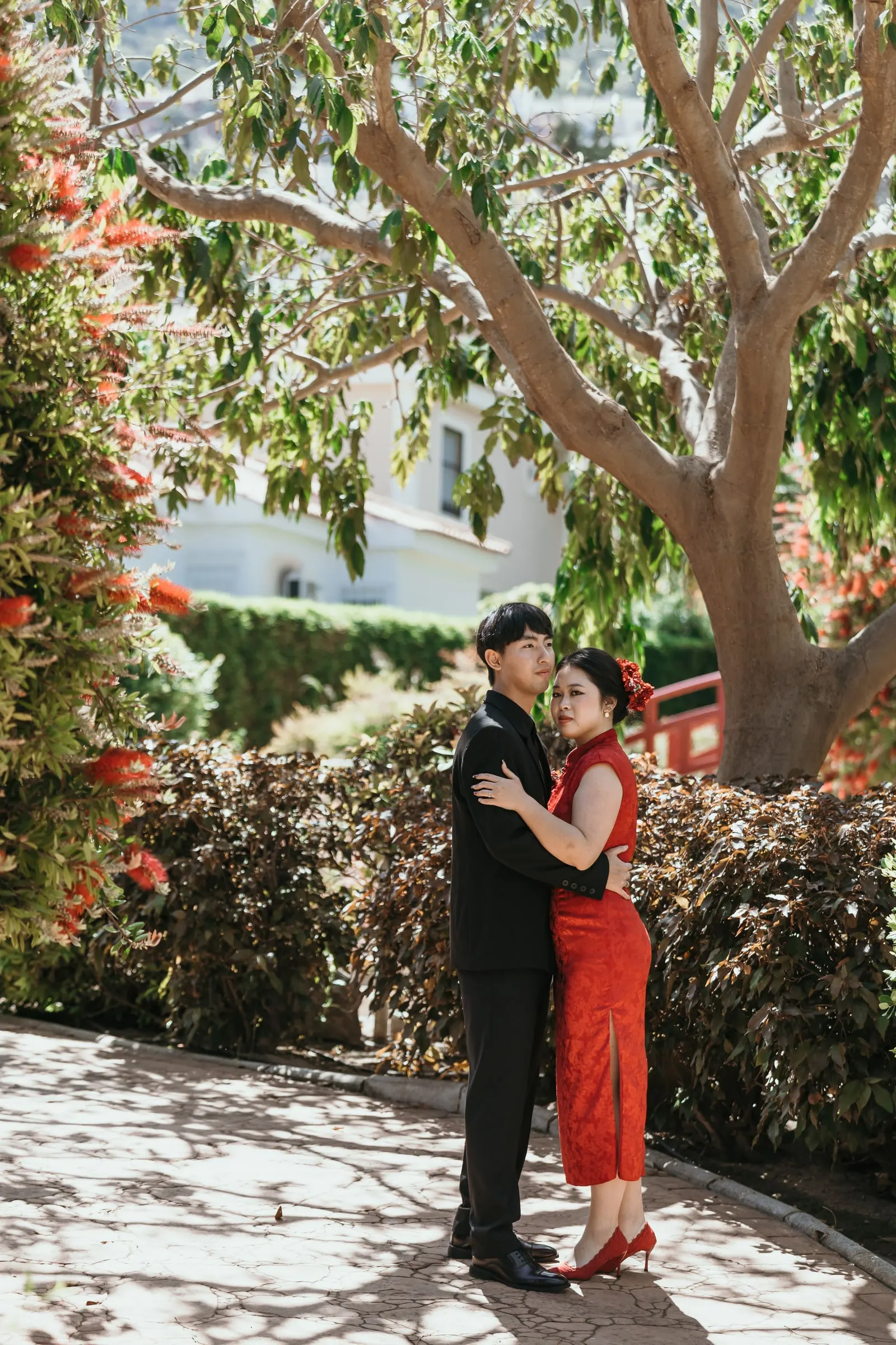Couple embracing and looking at the camera beside red flowering shrubs in Alhaurín de la Torre