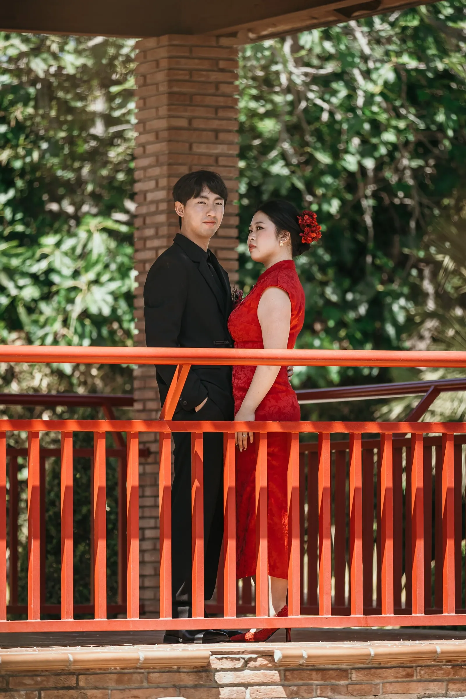 Couple standing side by side at the red railing of the pagoda, a red flower in her hair