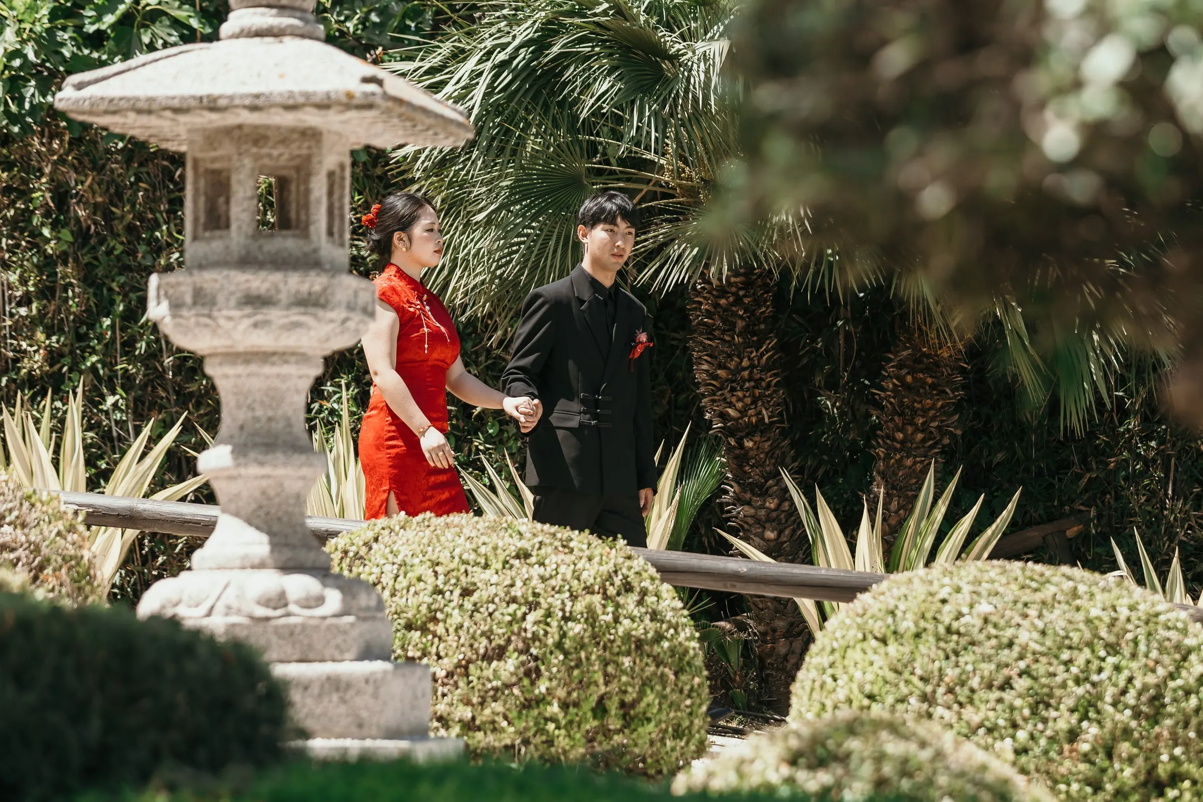 Couple walking past a stone lantern among rounded shrubs in the Japanese garden of Alhaurín de la Torre