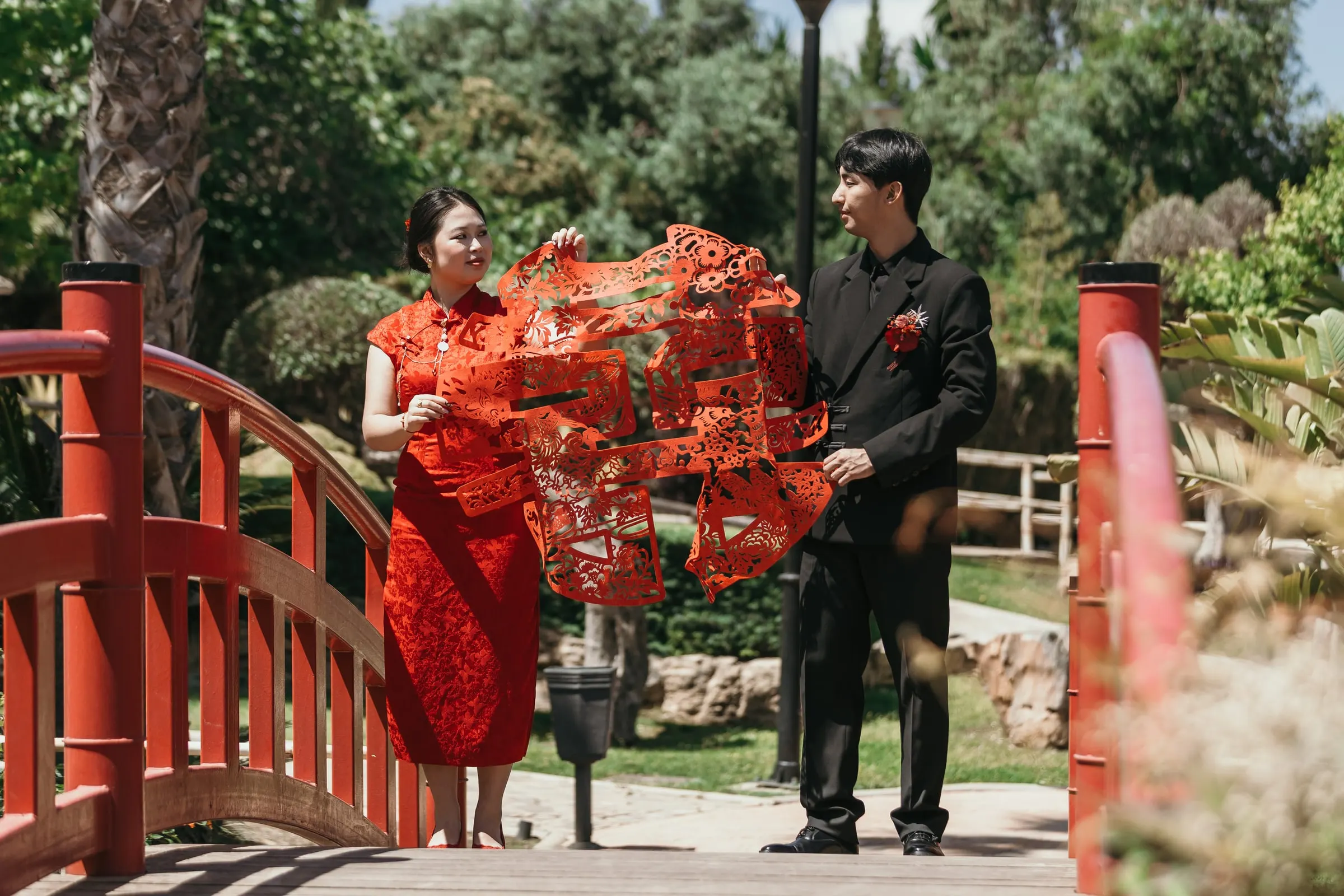Couple holding up a red double happiness paper-cut on a red arched bridge, pre-wedding session in Alhaurín de la Torre