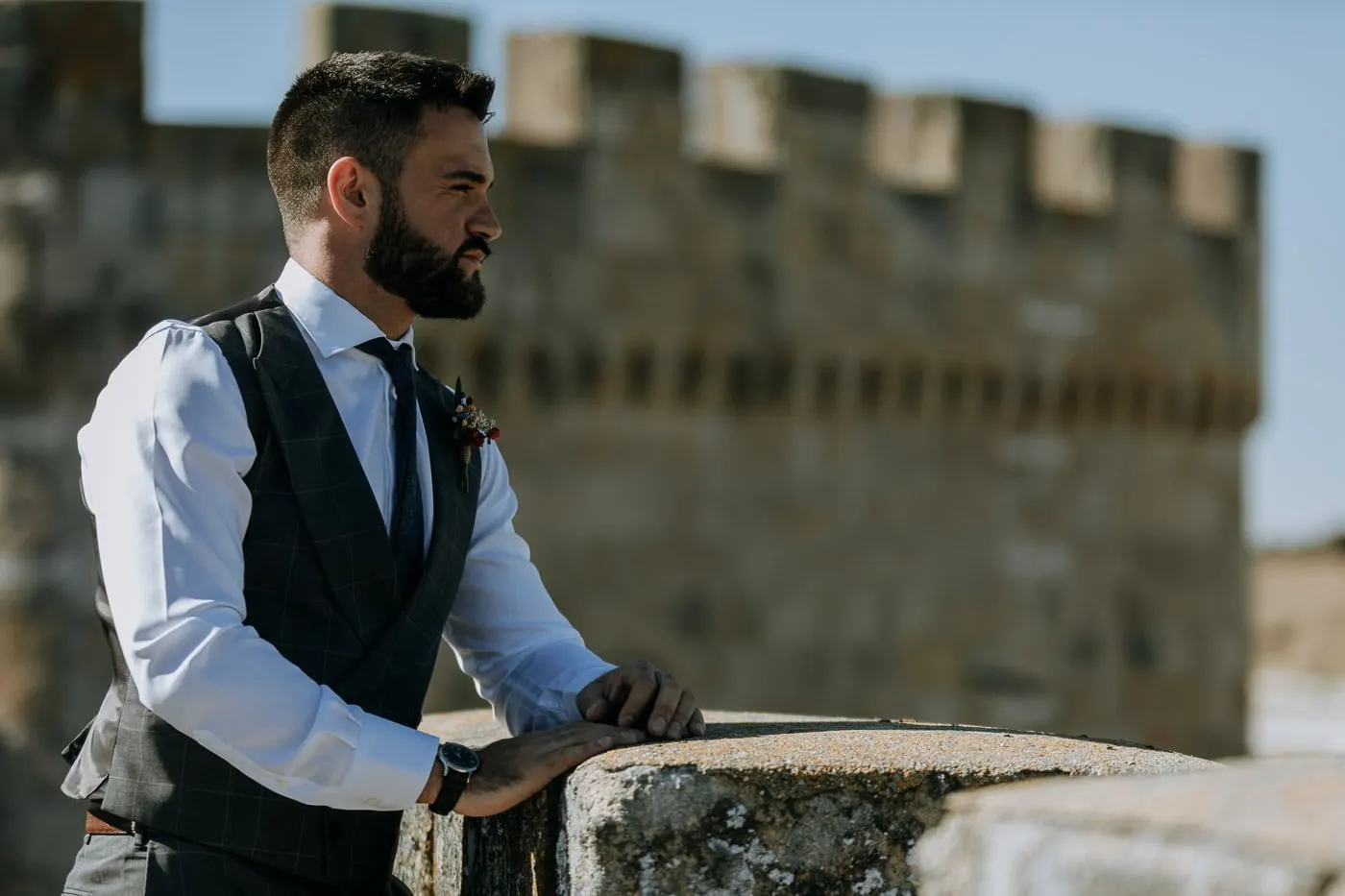 Groom in a waistcoat leaning on the battlements with the castle tower behind, Salamanca