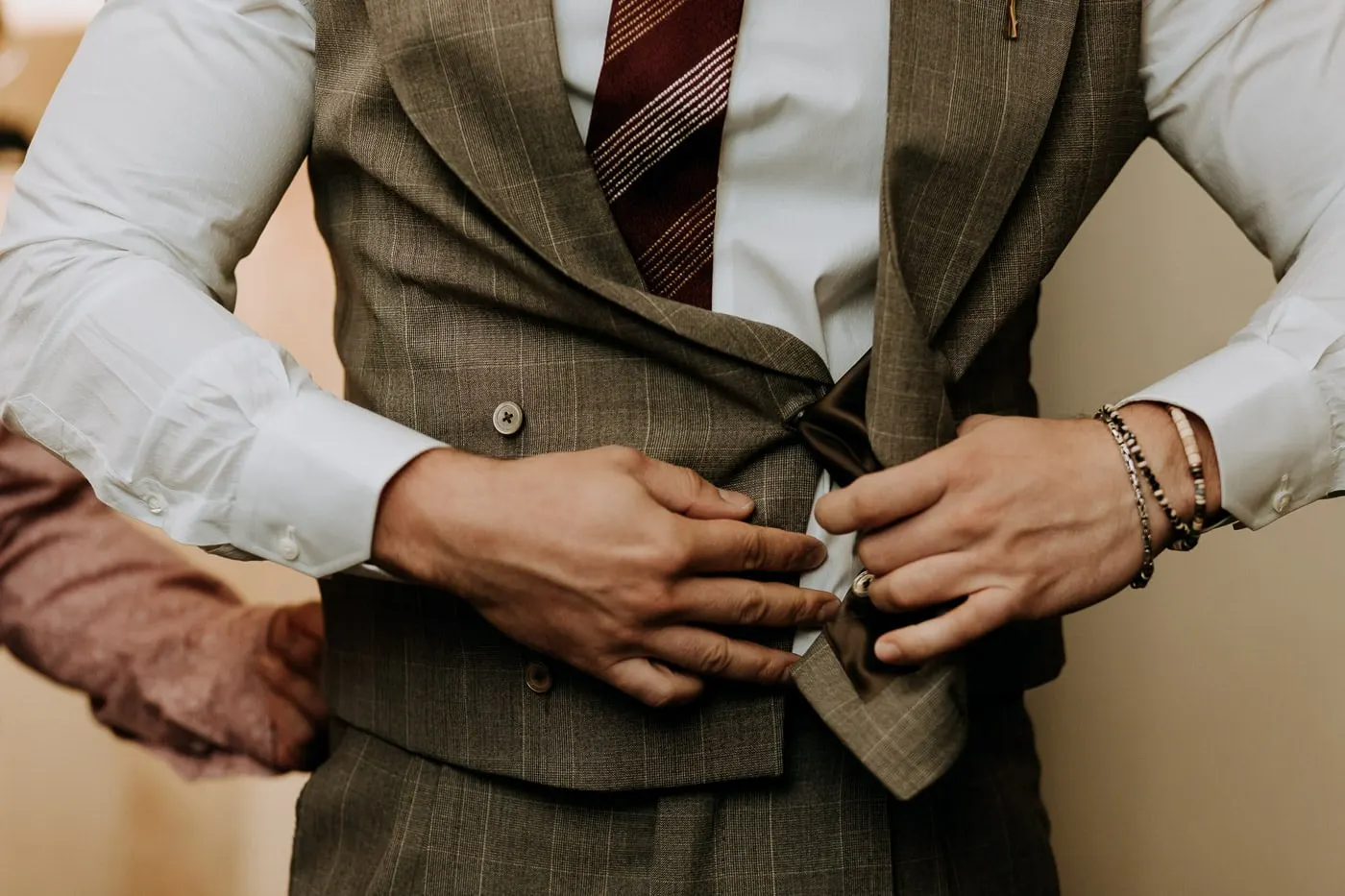 Detail of hands buttoning a brown check double-breasted waistcoat, Salamanca