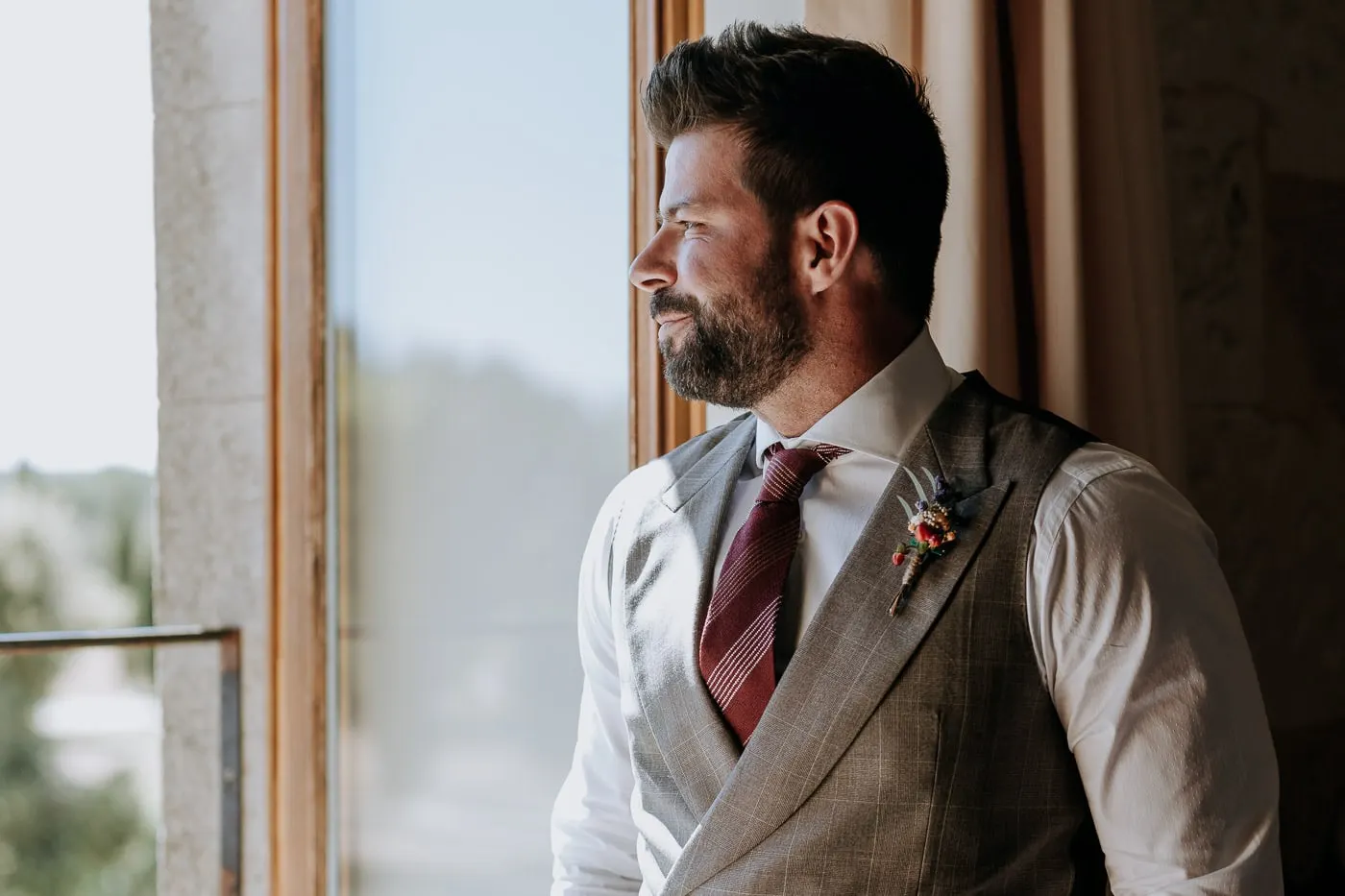 Groom in a check waistcoat and burgundy tie looking out of the window, Castillo del Buen Amor
