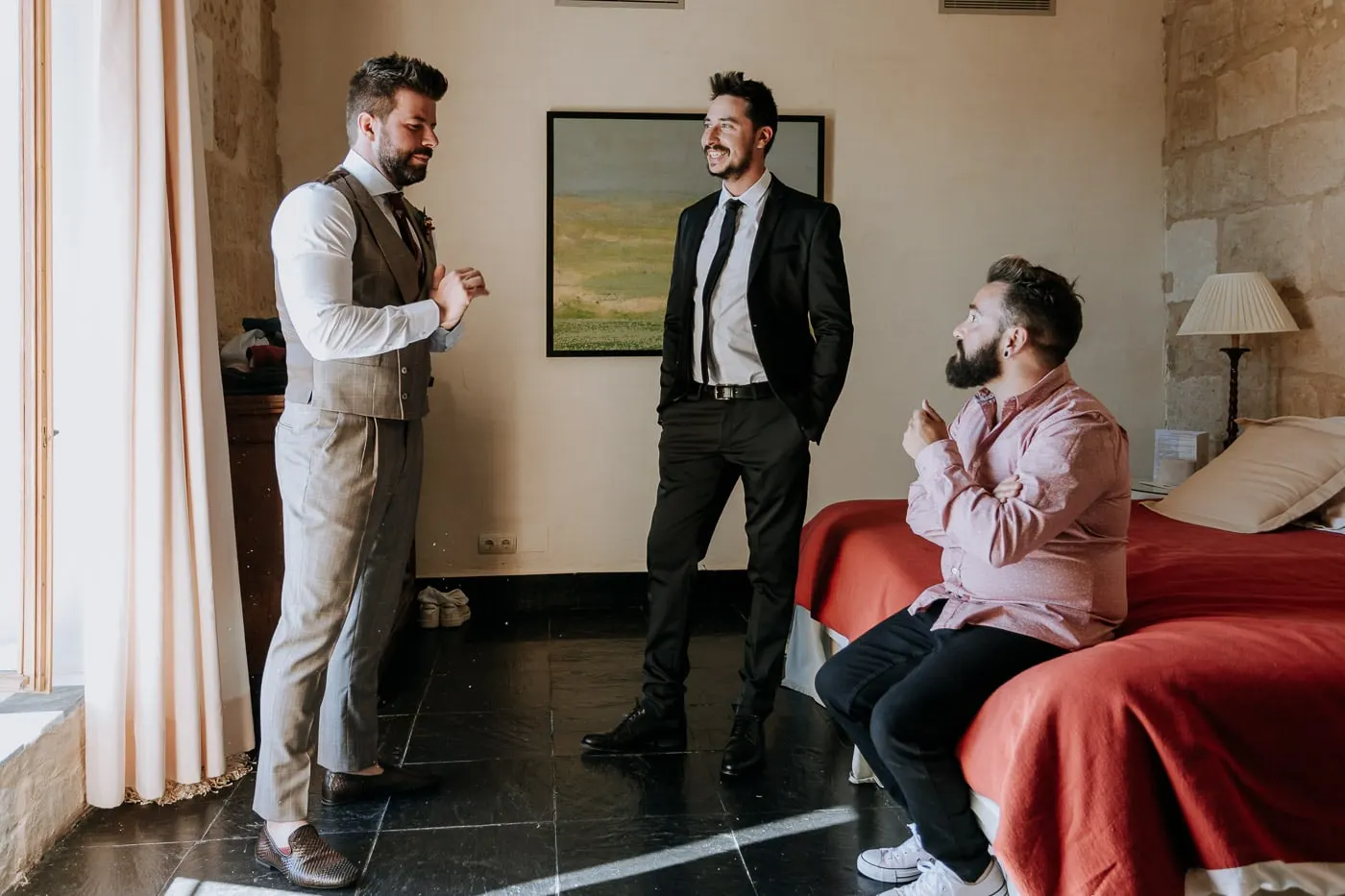 Groom and two friends chatting in a castle bedroom with a red bedspread, Salamanca