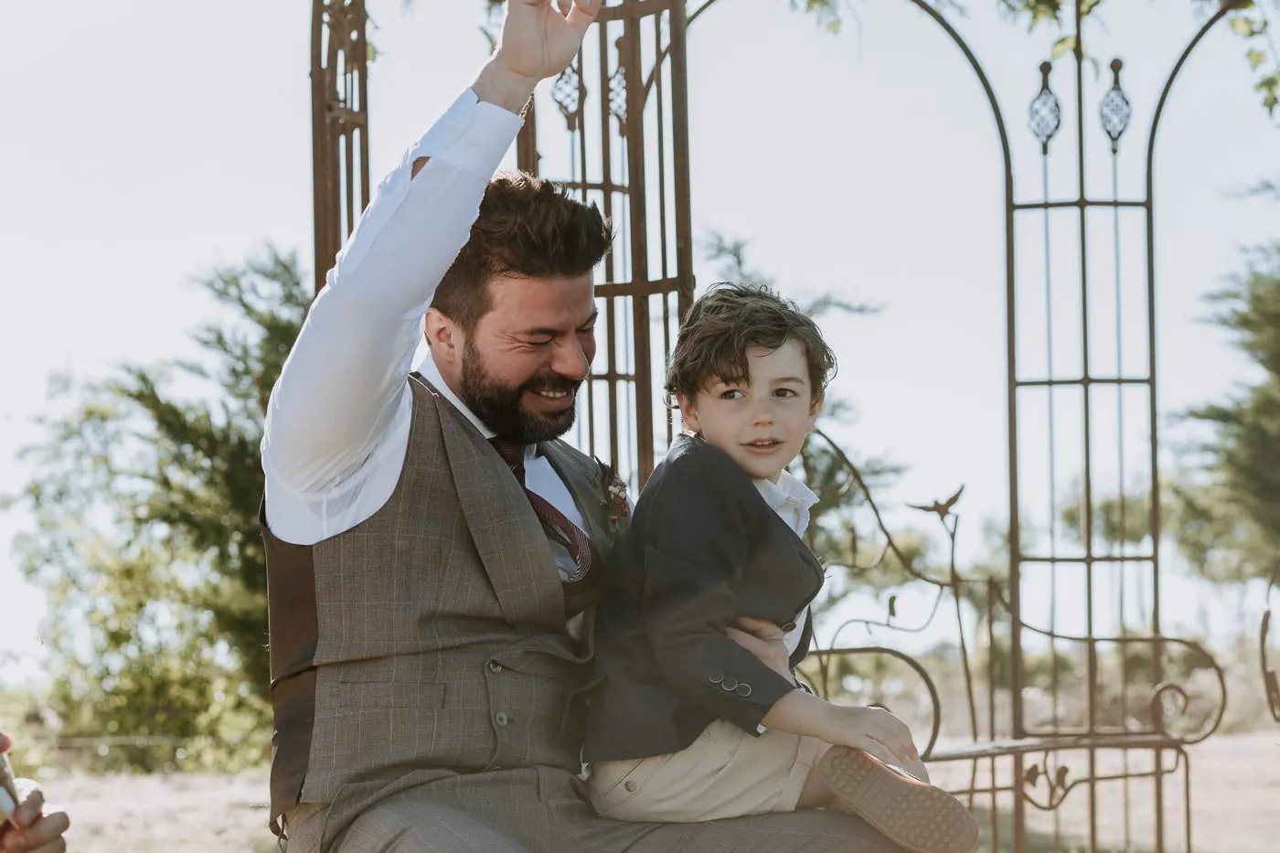 Groom raising his arm and laughing with the boy on his lap, Castillo del Buen Amor