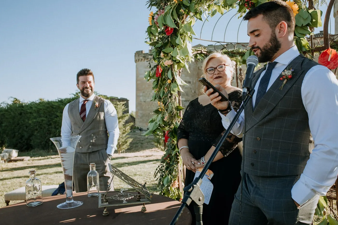 Groom speaking at the microphone as the other listens by the gazebo, Castillo del Buen Amor