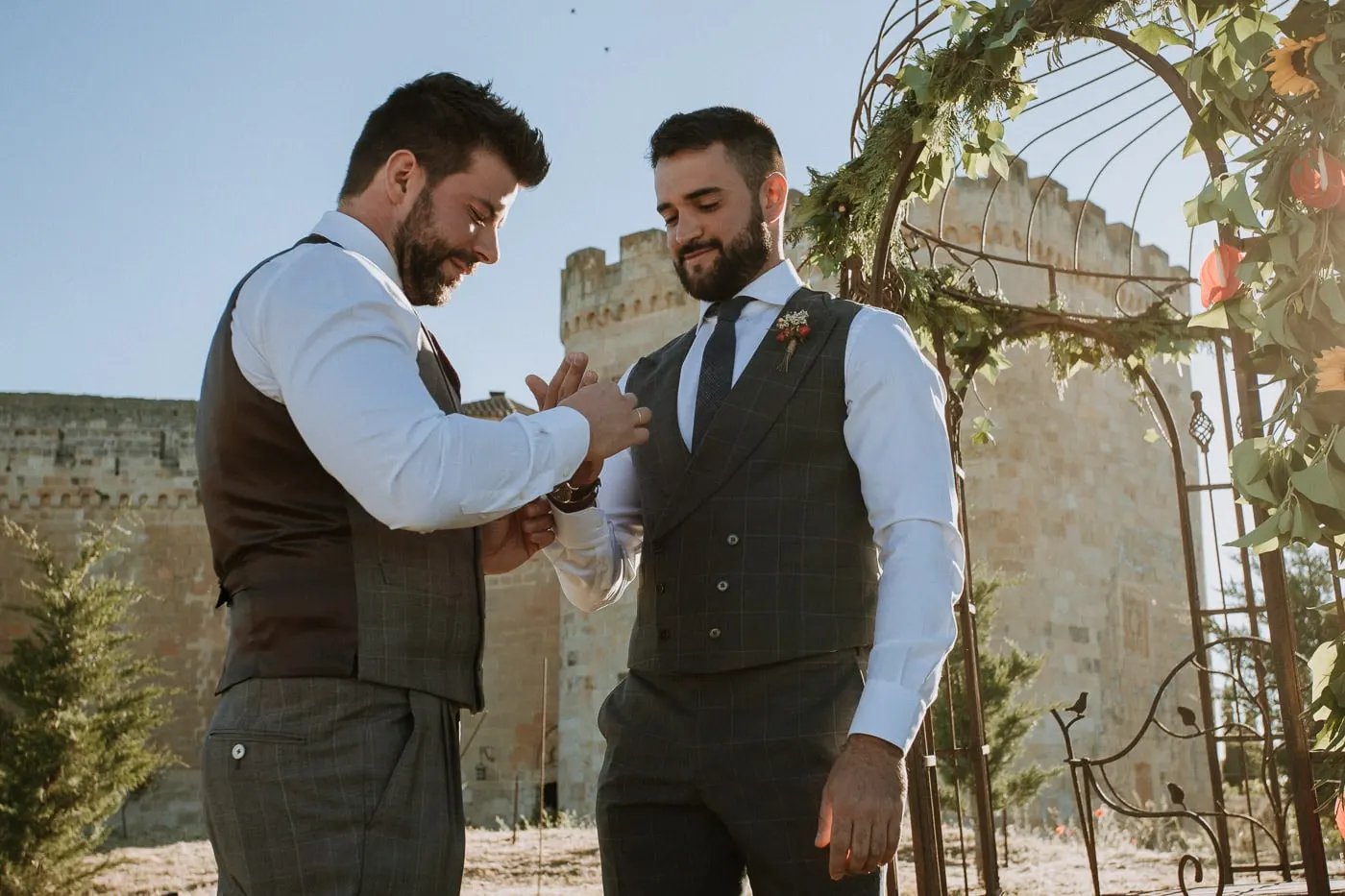 The grooms exchanging rings by the iron gazebo with the castle walls behind, Castillo del Buen Amor