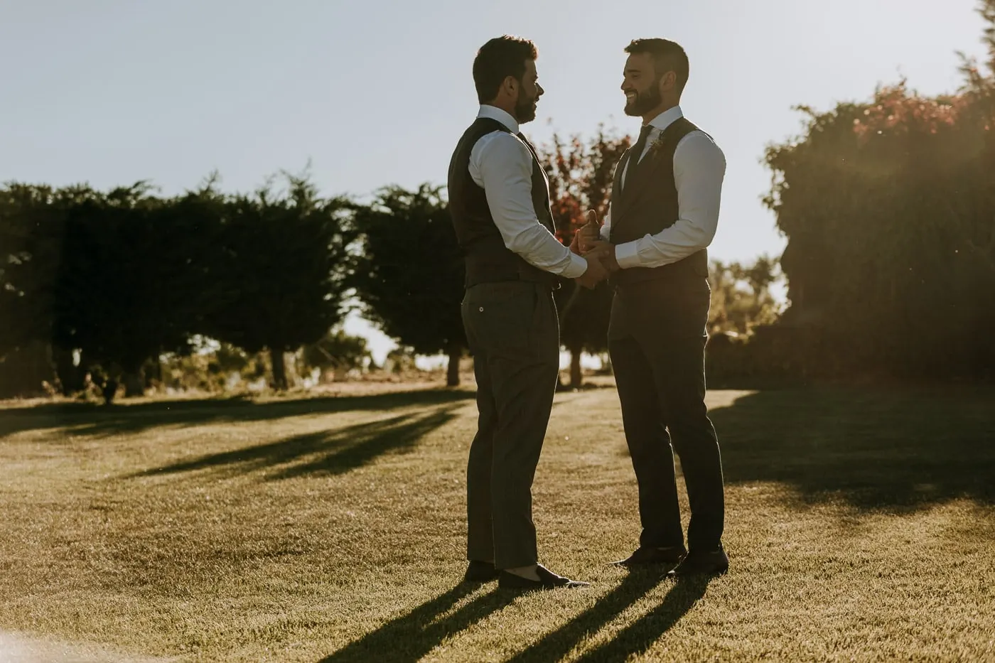The grooms holding hands on the lawn in the evening light, Castillo del Buen Amor