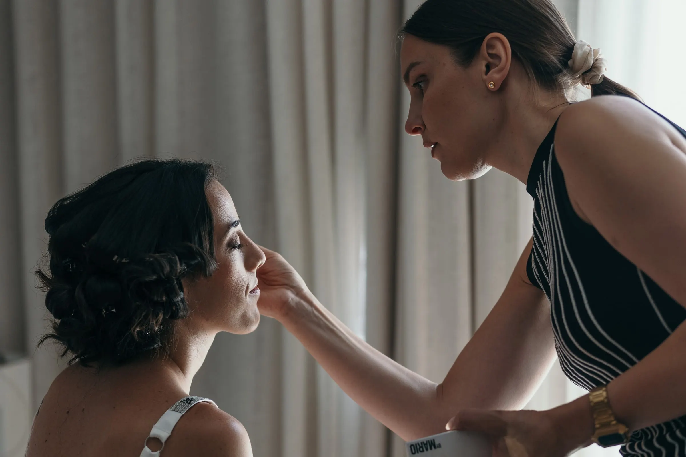 The make-up artist touches up Sara's face by the curtains of her hotel room in Ronda