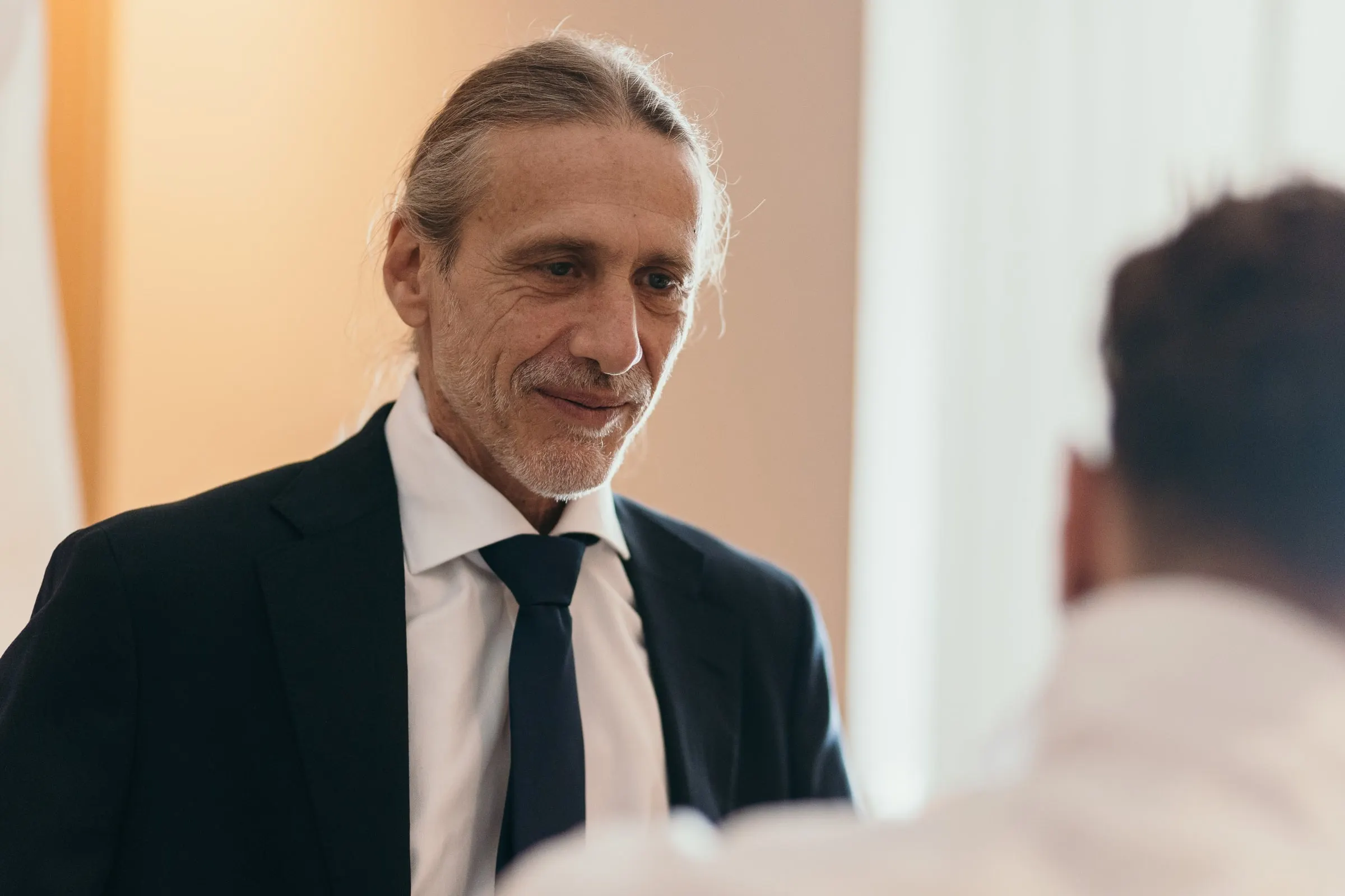 Un invitado sonriente, de traje oscuro y corbata, durante los preparativos