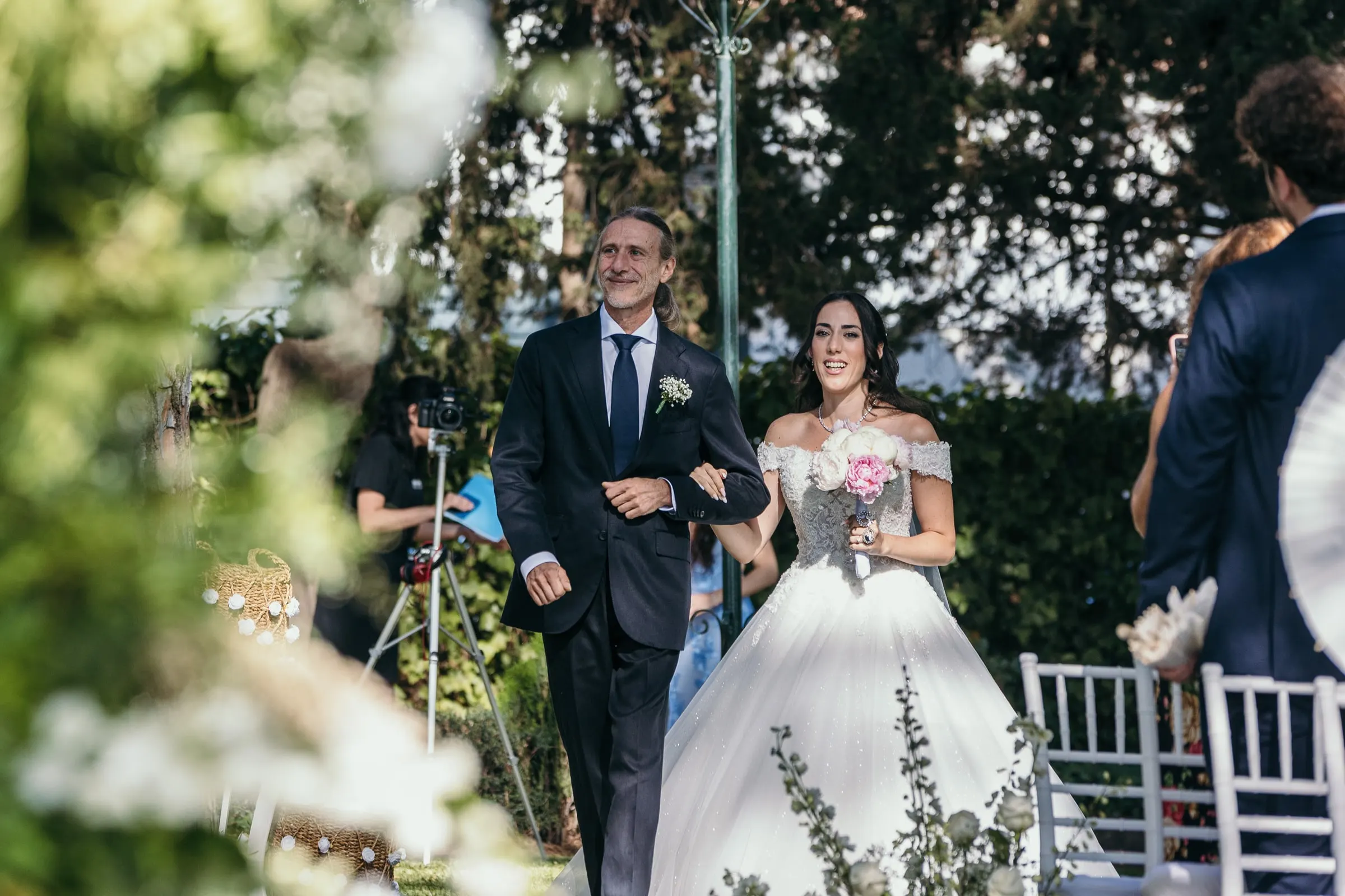 Sara avanza por el pasillo entre flores blancas, del brazo de un hombre de traje azul