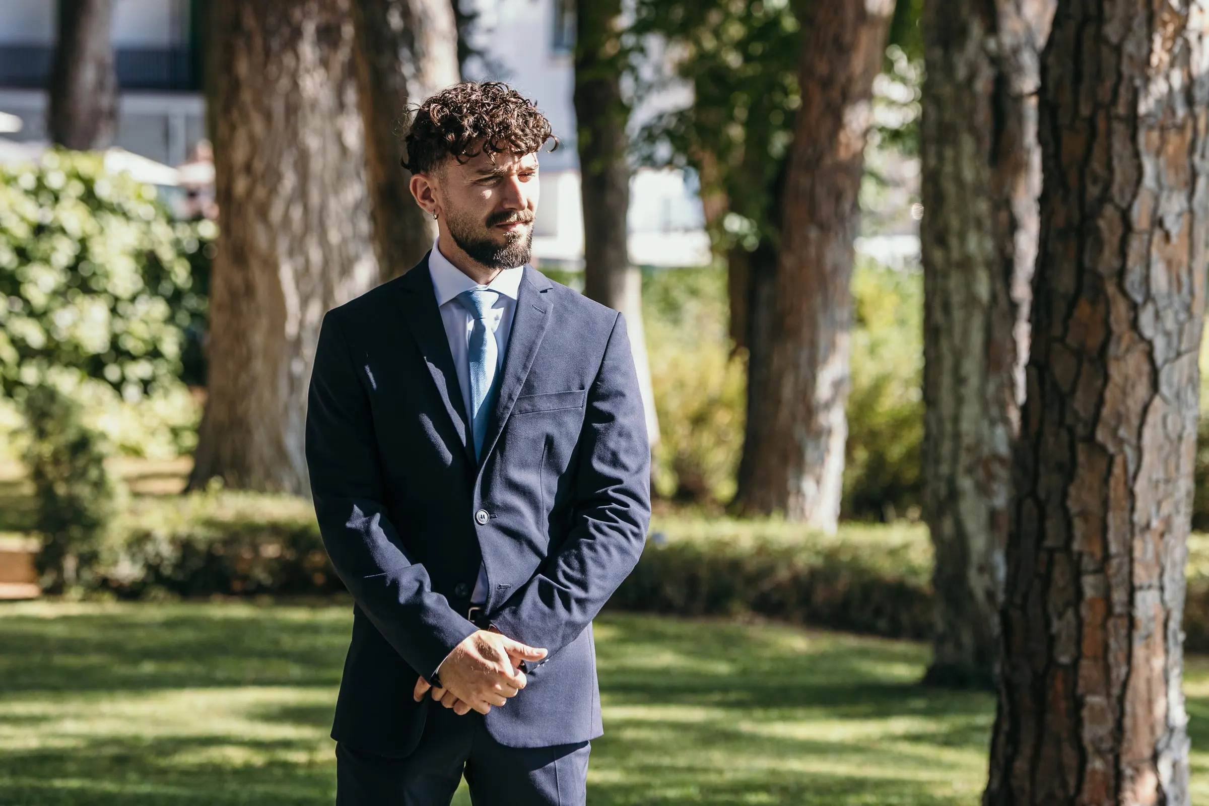 Vincent espera solo en el césped bajo los pinos altos antes de la ceremonia