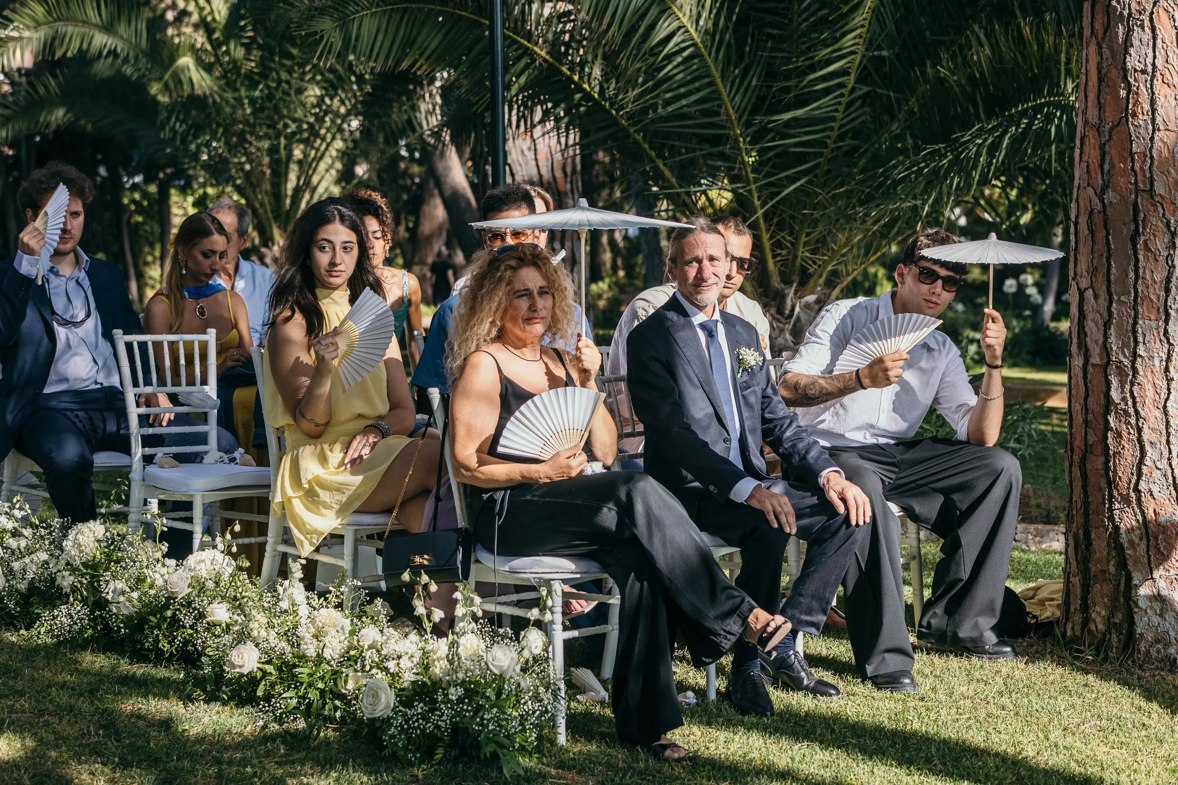 Invitados con ropa de verano sentados a la sombra de los árboles para la ceremonia en el jardín