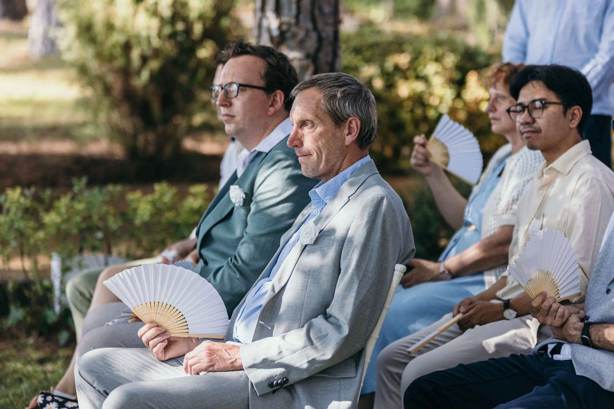 Invitados con abanicos blancos de papel escuchan la ceremonia en el jardín del hotel