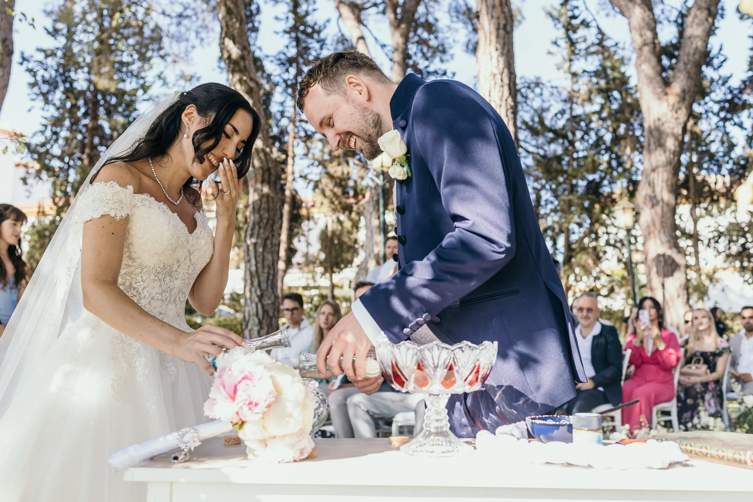 Sara y Vincent vierten juntos arena de colores en la mesa de la ceremonia, bajo los pinos