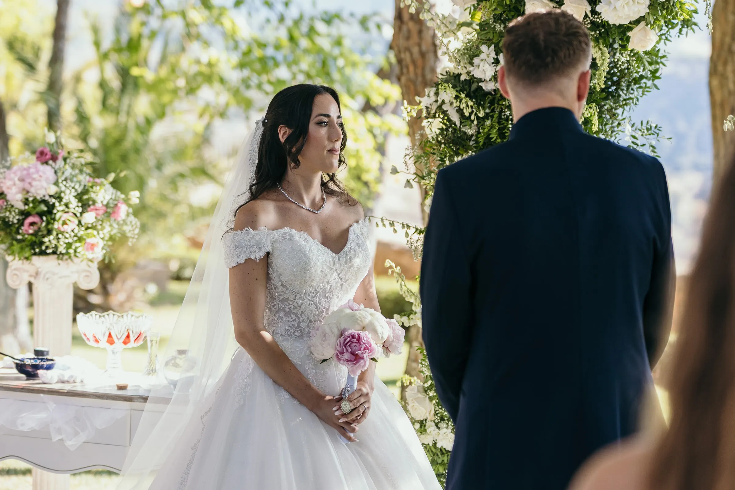 Sara frente a Vincent en el altar, con un ramo de peonías rosas y blancas