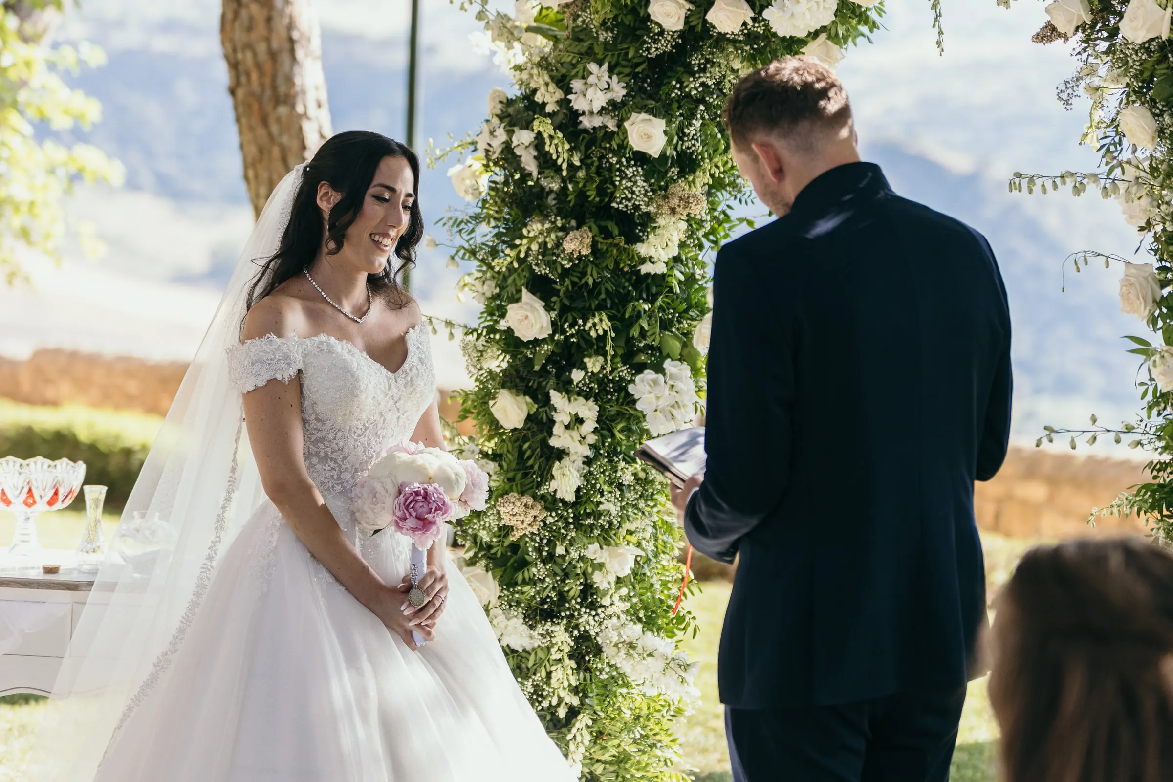 Sara escucha mientras Vincent lee junto al arco de rosas blancas