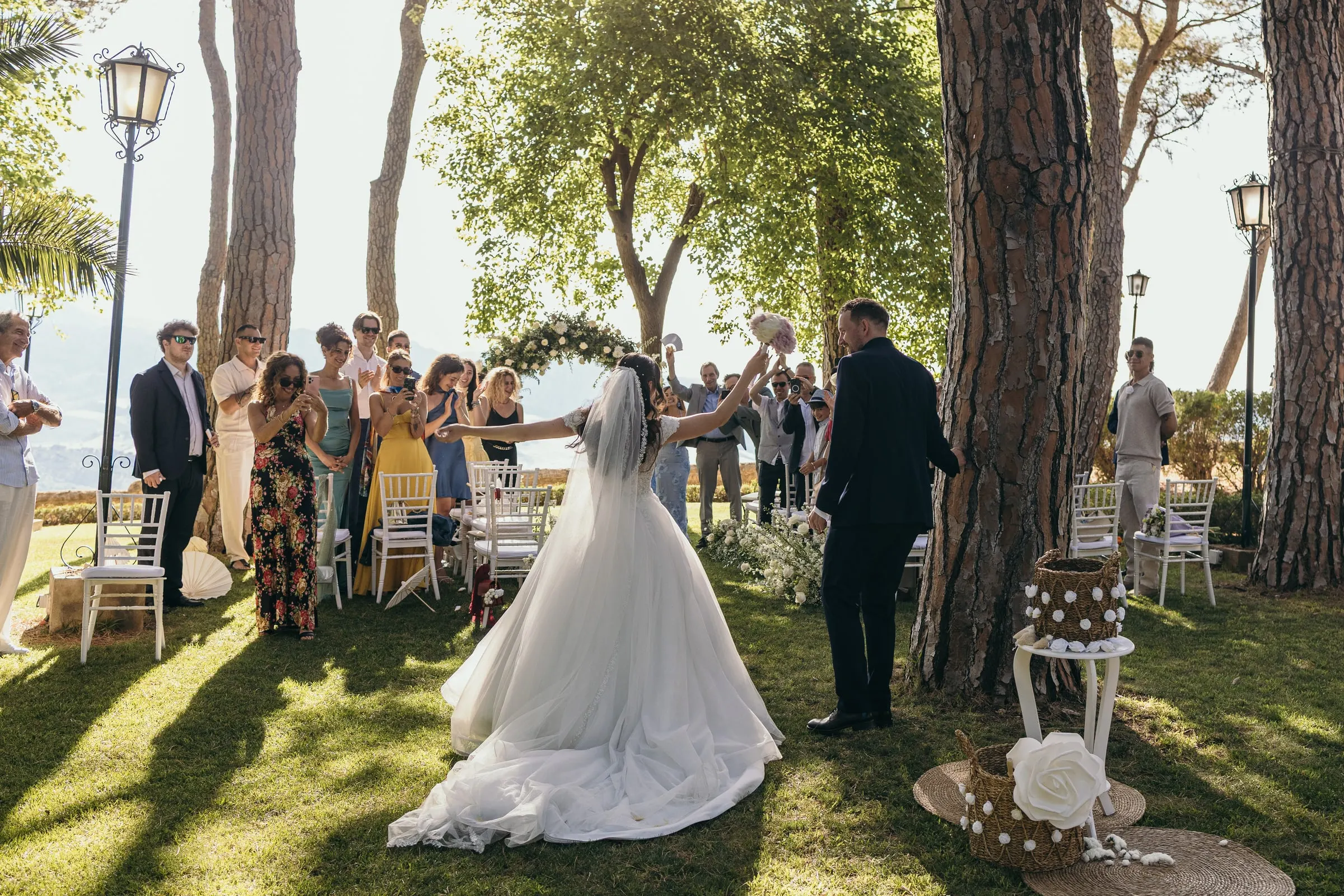 El velo largo de Sara se arrastra por el césped mientras los invitados aplauden a los recién casados