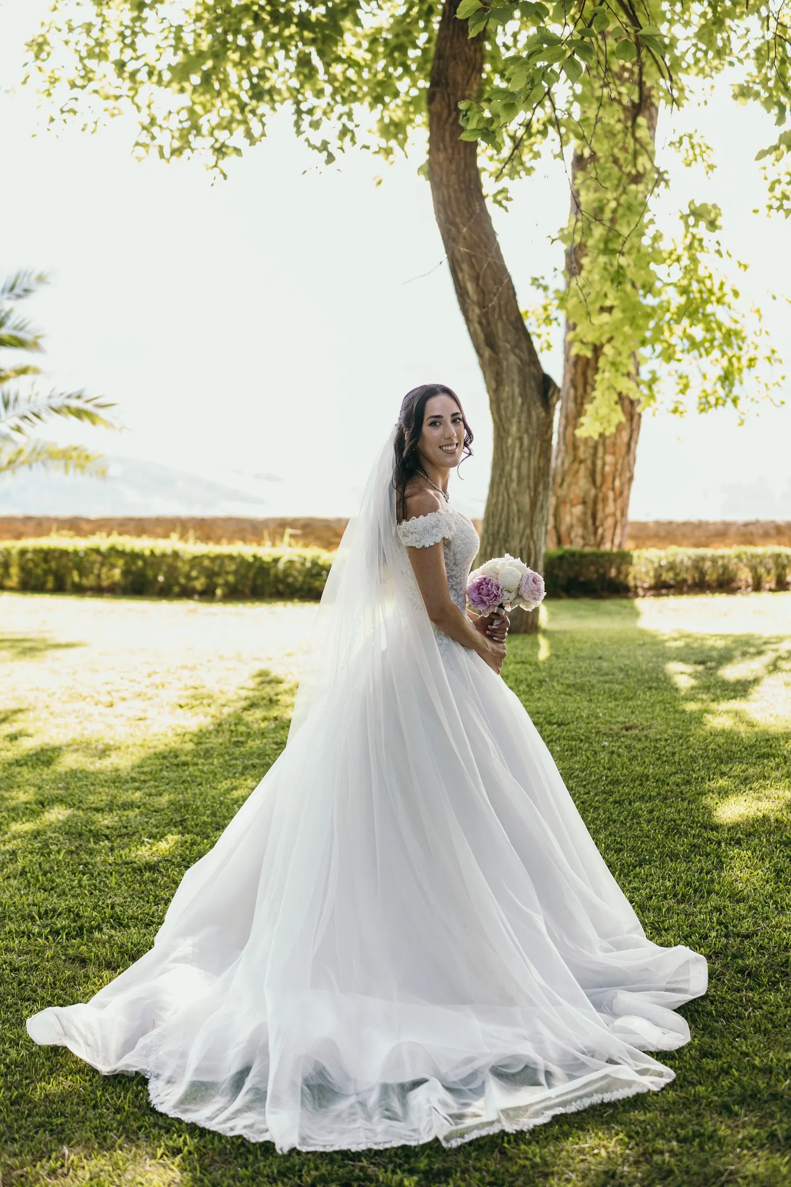 Sara, sola en el césped con su vestido de princesa, con el velo cayendo hasta la hierba