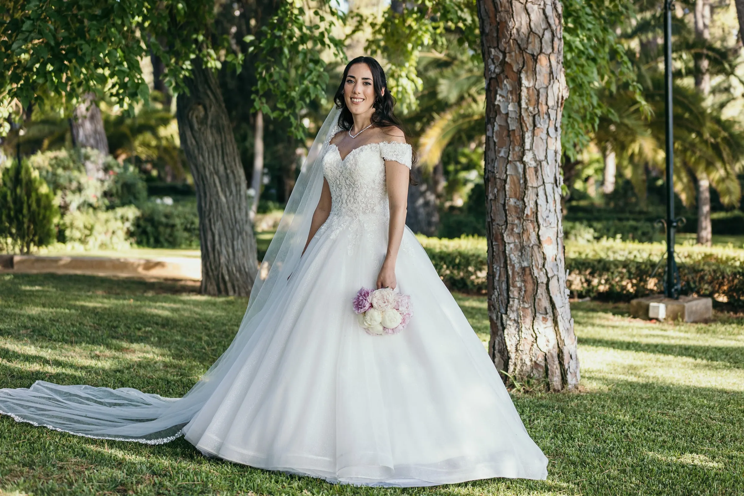 Sara con su ramo bajo los pinos y la cola del vestido extendida por la hierba