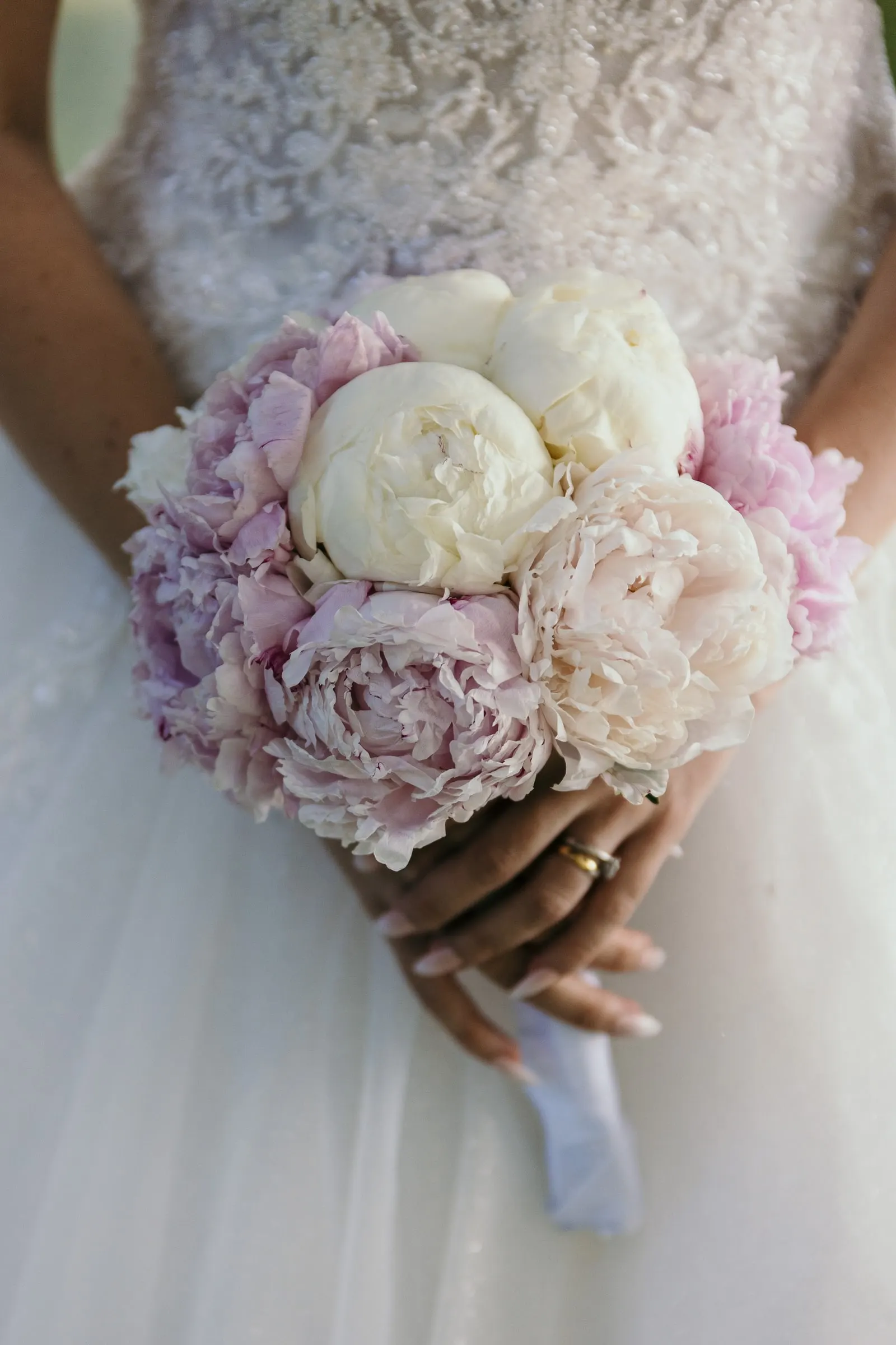 Detalle del ramo de peonías blancas y rosas de Sara sobre el encaje del vestido