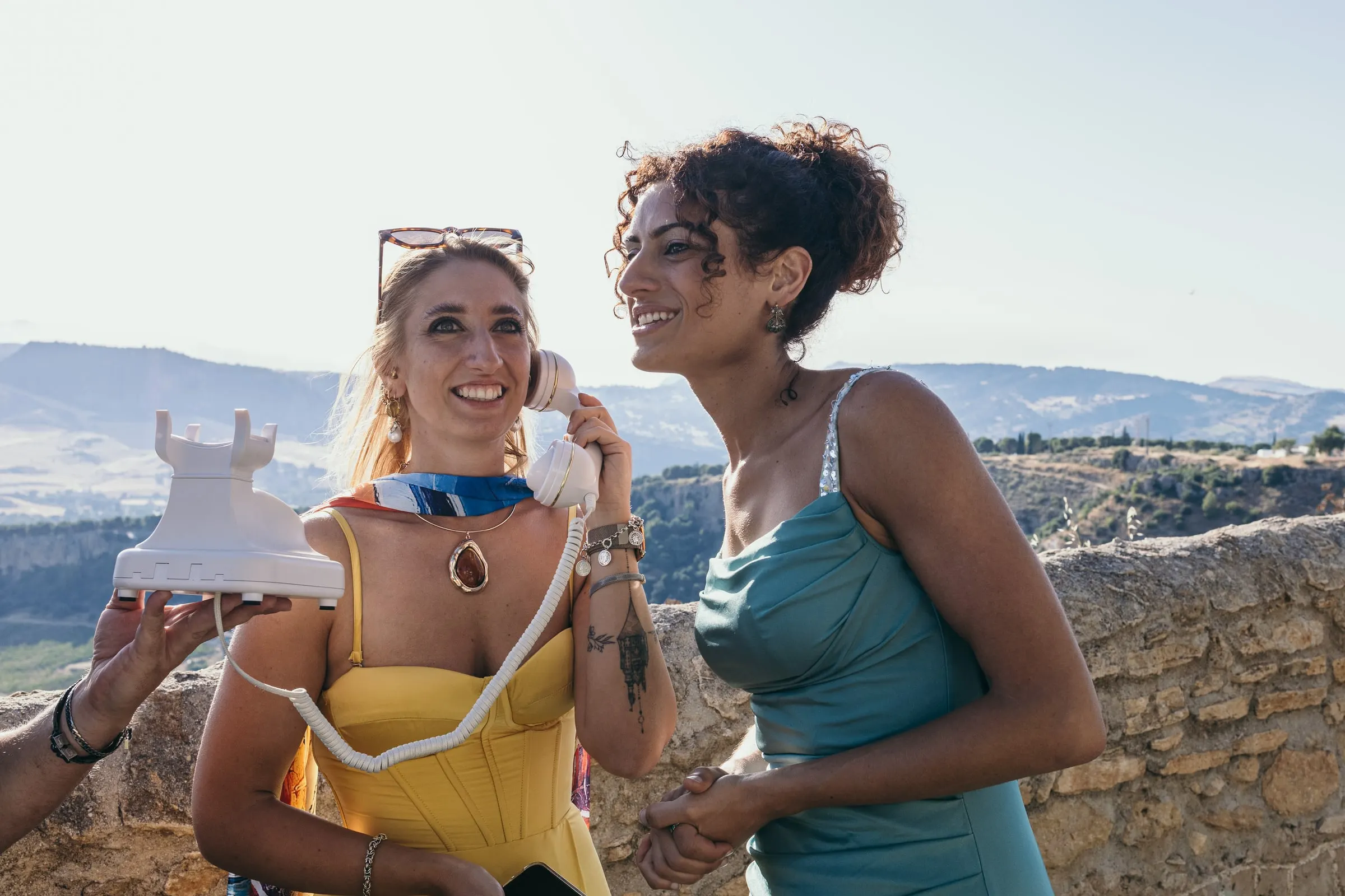Dos invitadas se ríen al teléfono del libro de invitados de audio junto al muro de la terraza