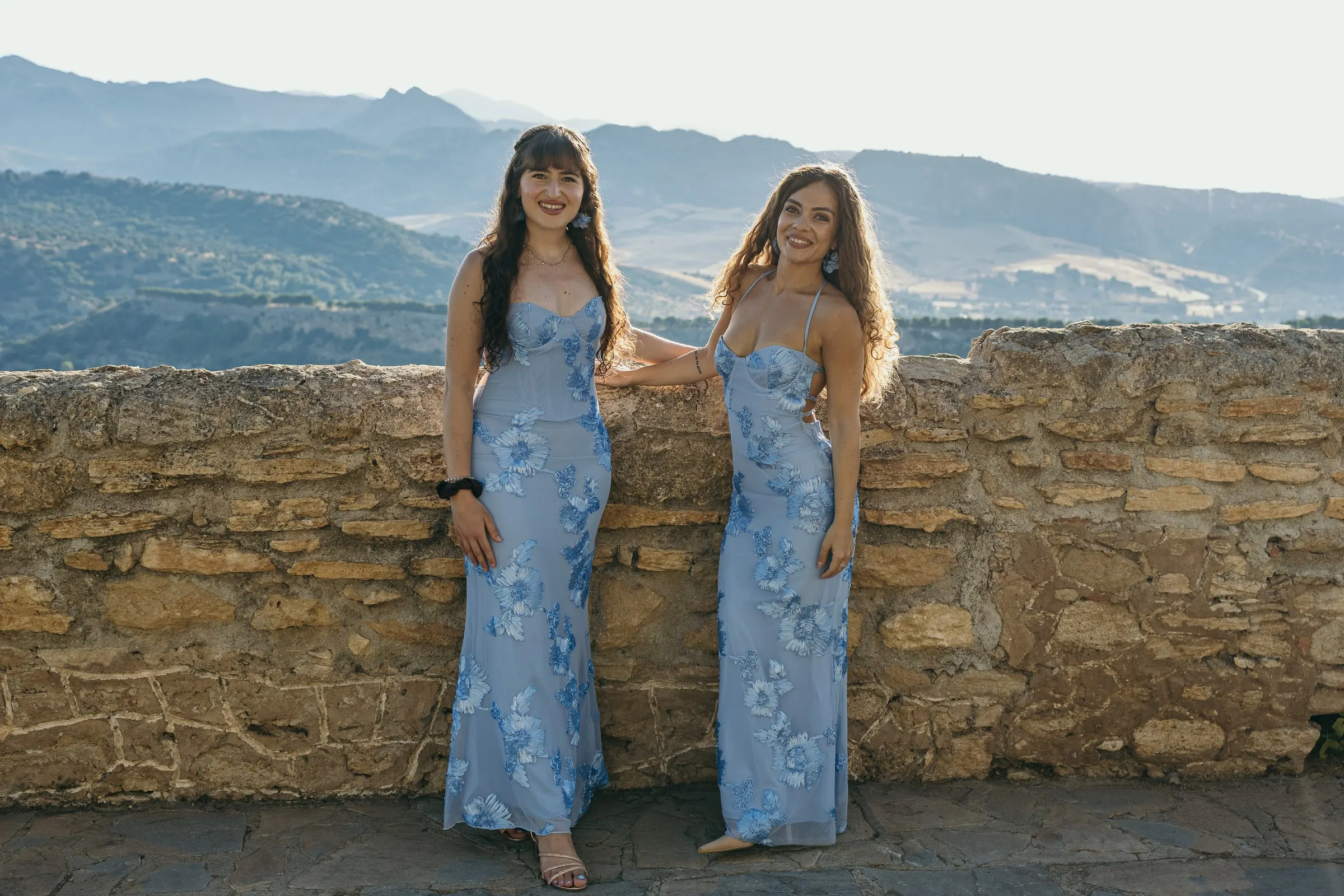 The bridesmaids in blue lean on the stone wall with the Serranía de Ronda behind