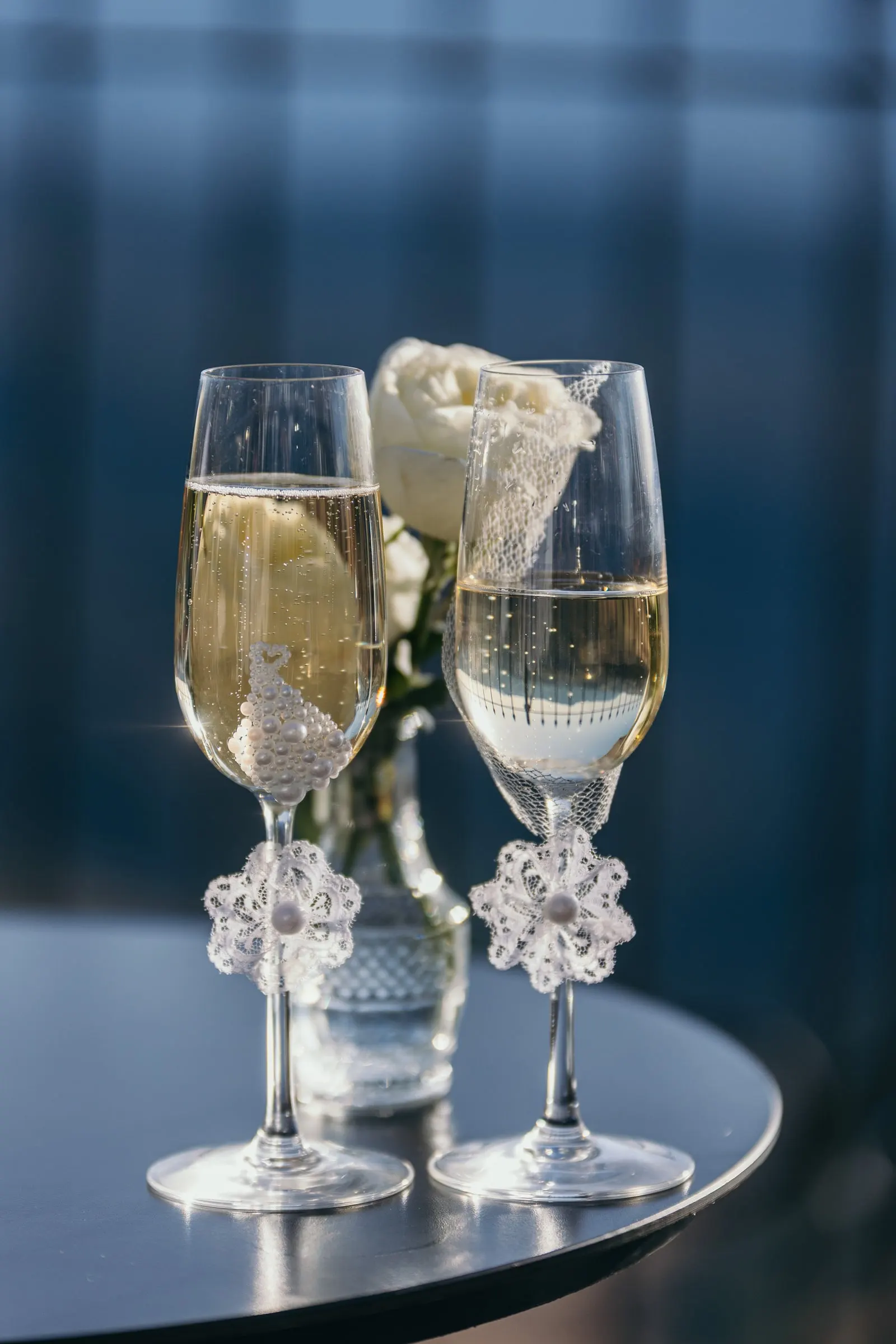Dos copas de cava con detalles de encaje y una rosa blanca sobre una mesa oscura