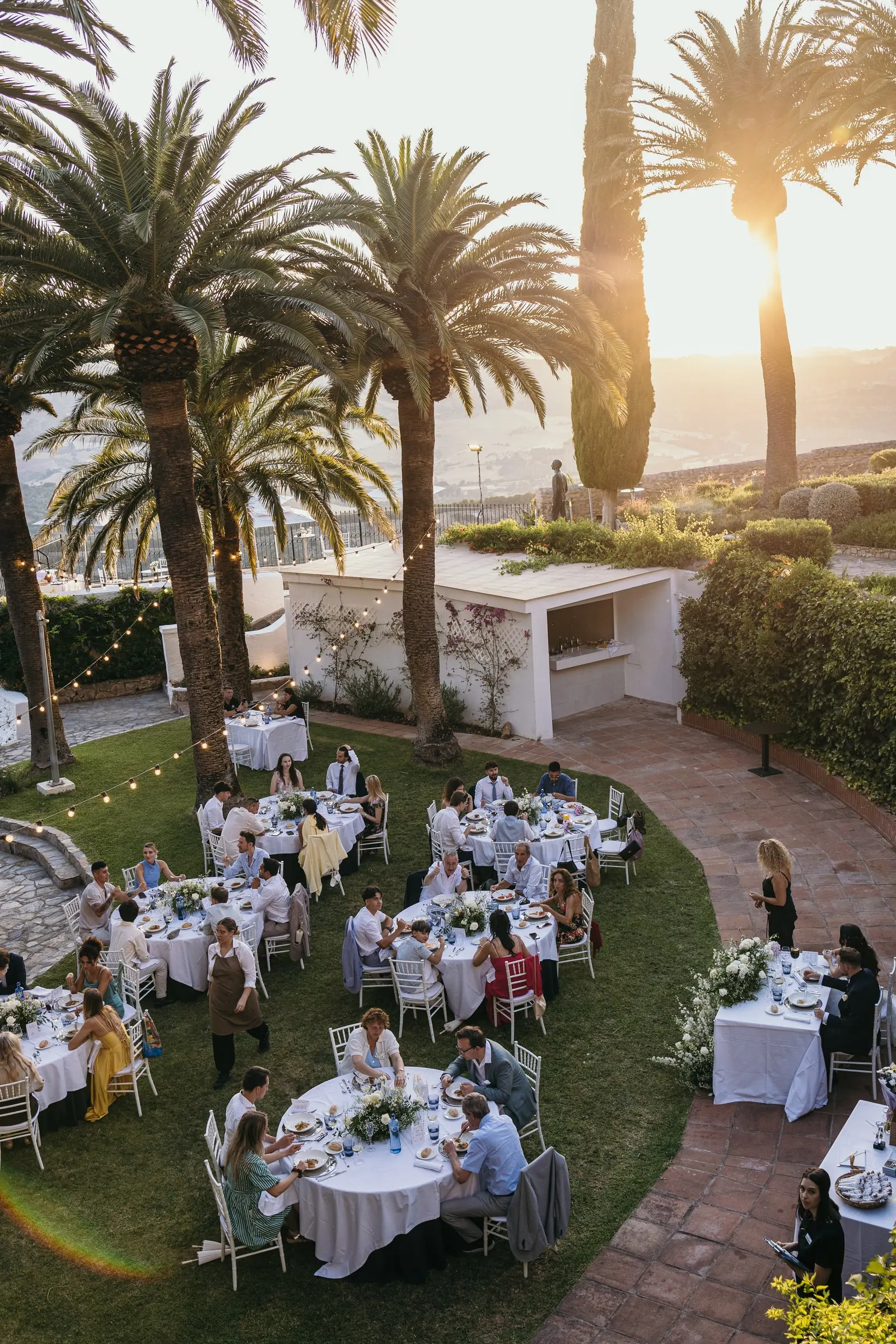 Dinner tables on the lawn among the palms, seen from above at sunset