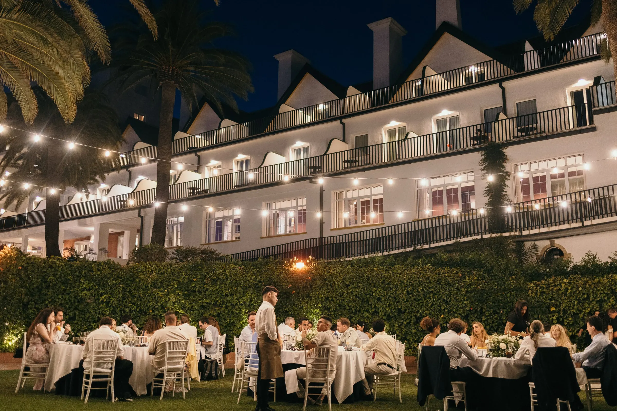 Cena en el jardín bajo guirnaldas de luces frente a la fachada blanca del Hotel Catalonia Reina Victoria, en Ronda